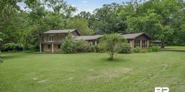 Image 4: Expansive green lawn presenting a stone and wood-sided residence with a covered second-story balcony
