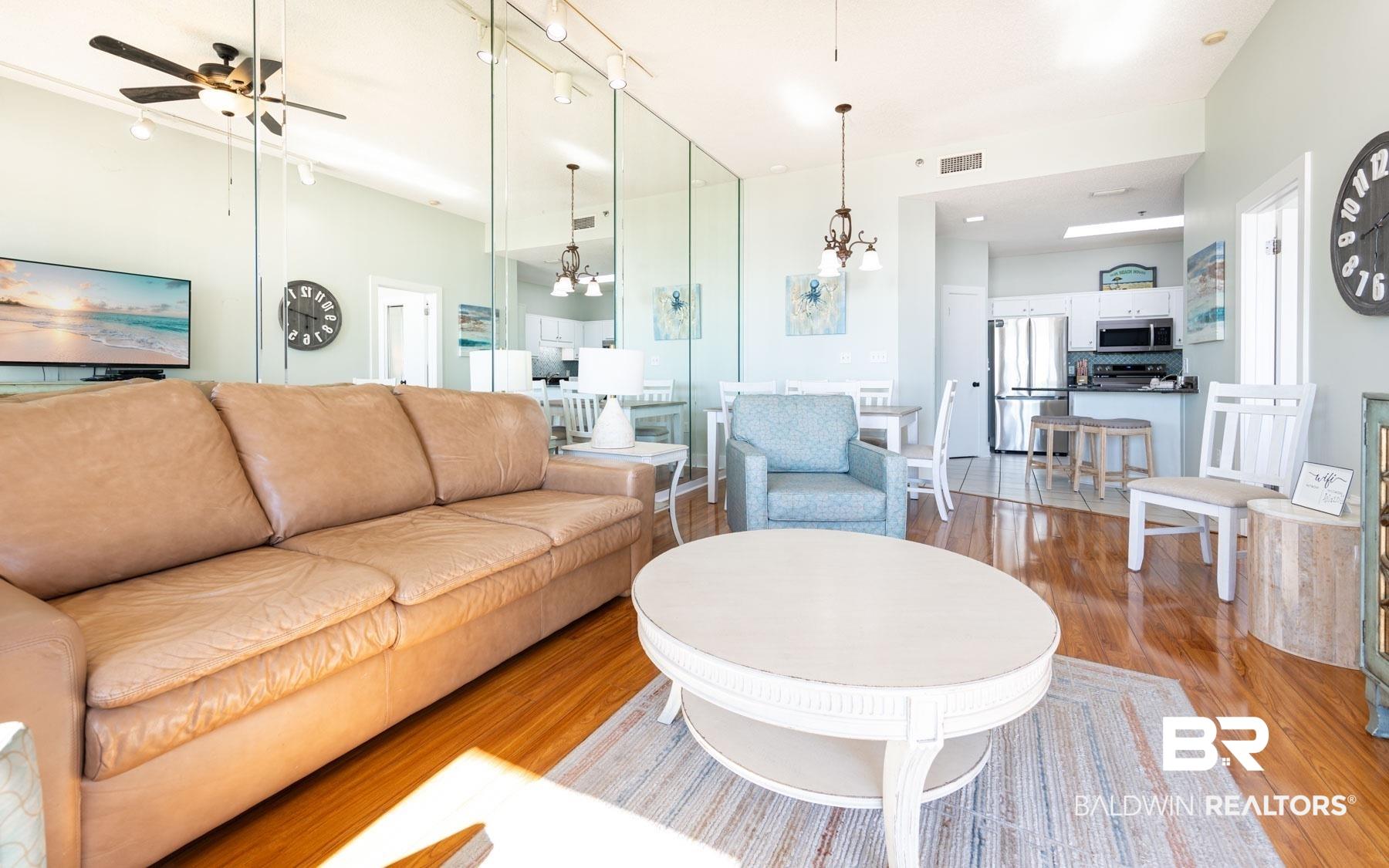 Image 3: Open-concept living space featuring wood-finish flooring, a contemporary ceiling fan, and mirrored wall accents