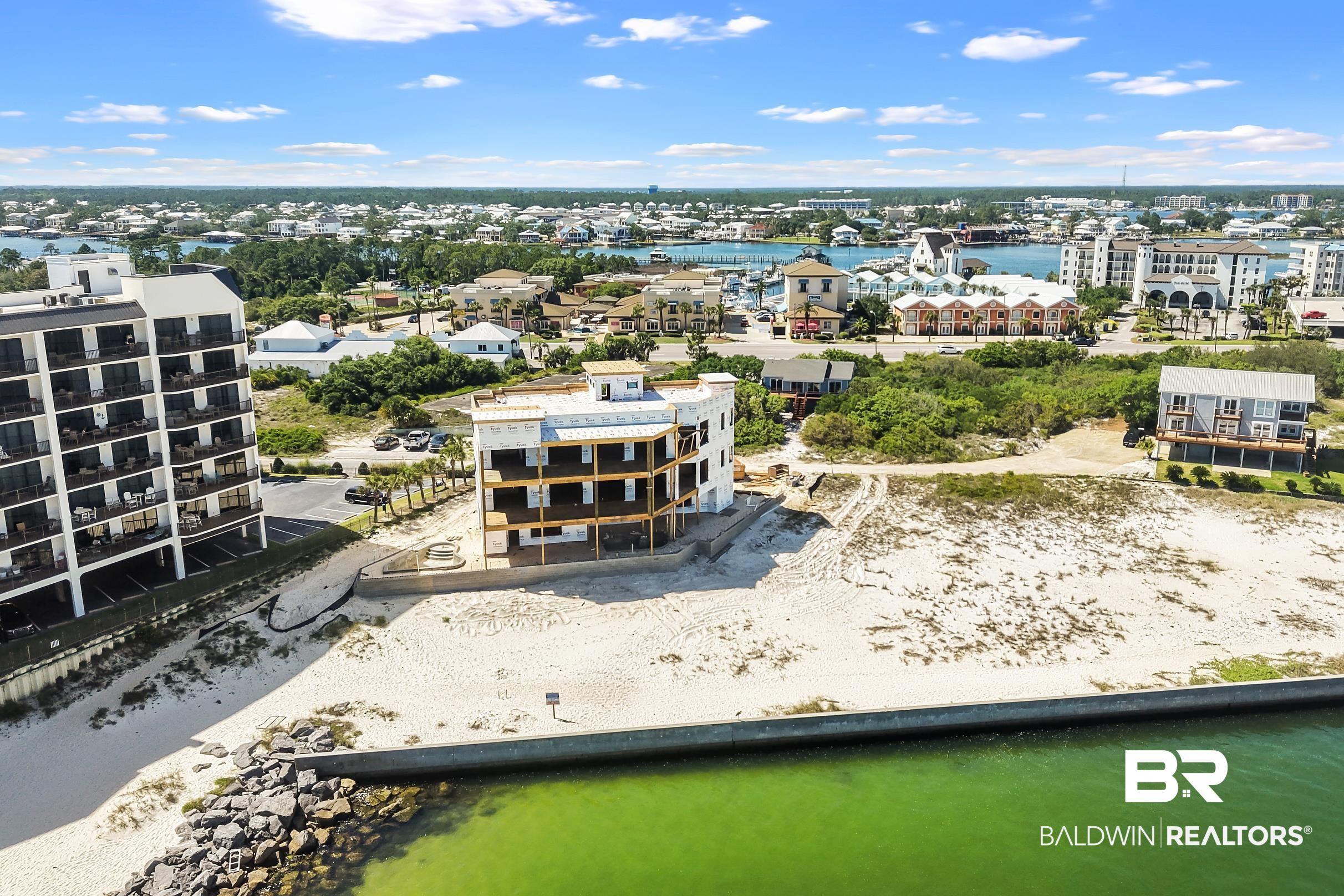 Image 2: Waterfront property featuring a partially constructed multi-story building, sandy ground, a concrete retaining wall, and a rocky shoreline