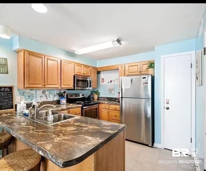 Image 4: Kitchen featuring stainless steel appliances, a kitchen breakfast bar, a peninsula, light tile patterned flooring, and dark stone countertops