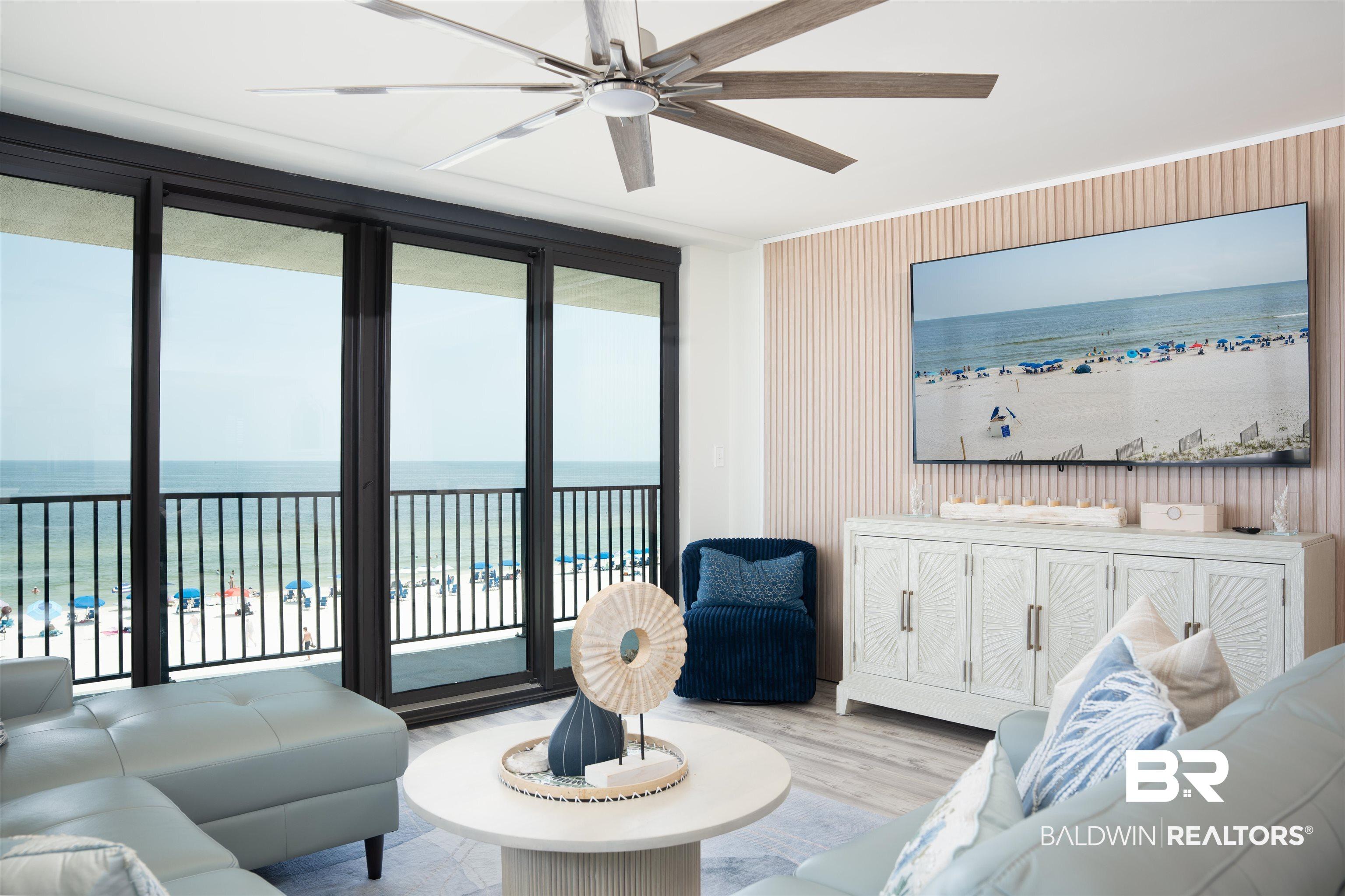 Image 3: Expansive sliding glass doors open to a balcony with black metal railings, overlooking a sandy beach and ocean