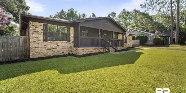 Image 2: Brick exterior featuring a covered front porch with dark wood railings and stairs