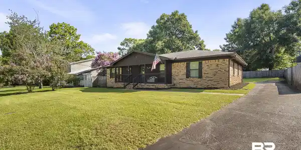 Image 3: Brick exterior with dark shutters, covered front porch, and mature landscaping