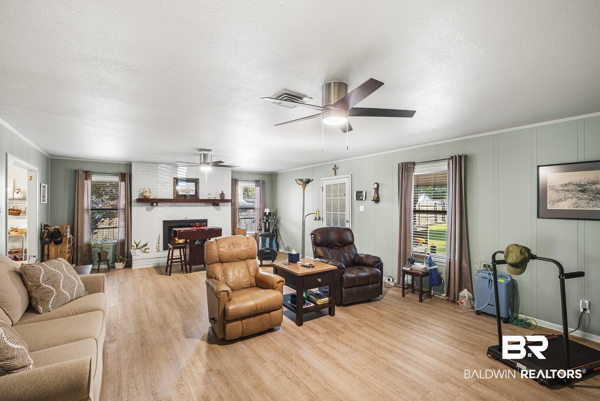 Image 4: Spacious living area featuring wood-finish flooring, a white-painted brick fireplace with a wood mantle, and two ceiling fans