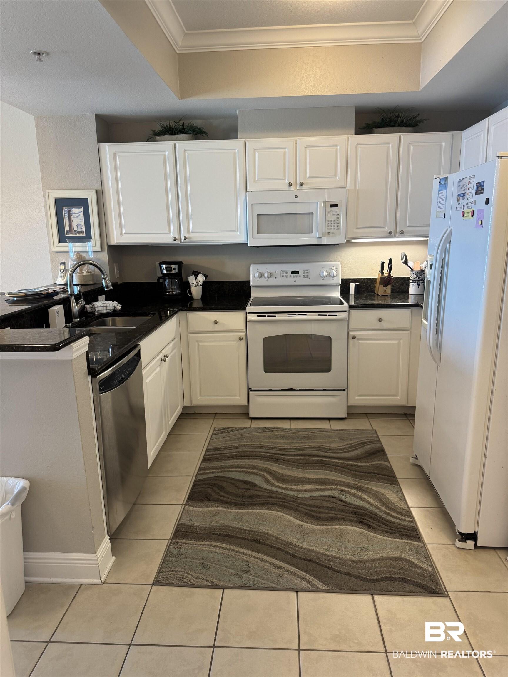 Image 4: Kitchen with white cabinets, crown molding, white appliances, a peninsula, and dark stone countertops