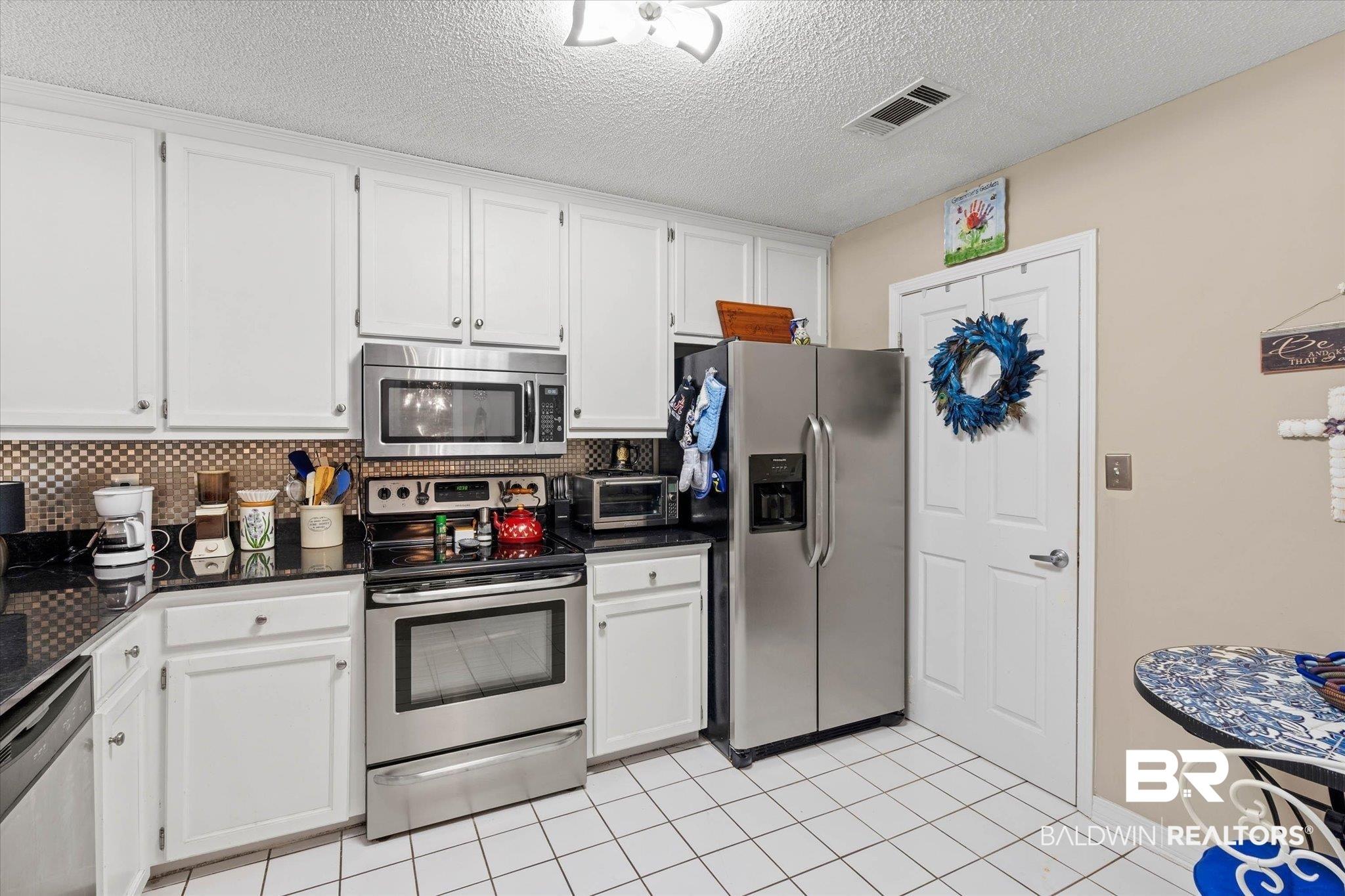 Image 3: Kitchen featuring white cabinetry, dark countertops, a stainless steel appliance suite, and a patterned backsplash