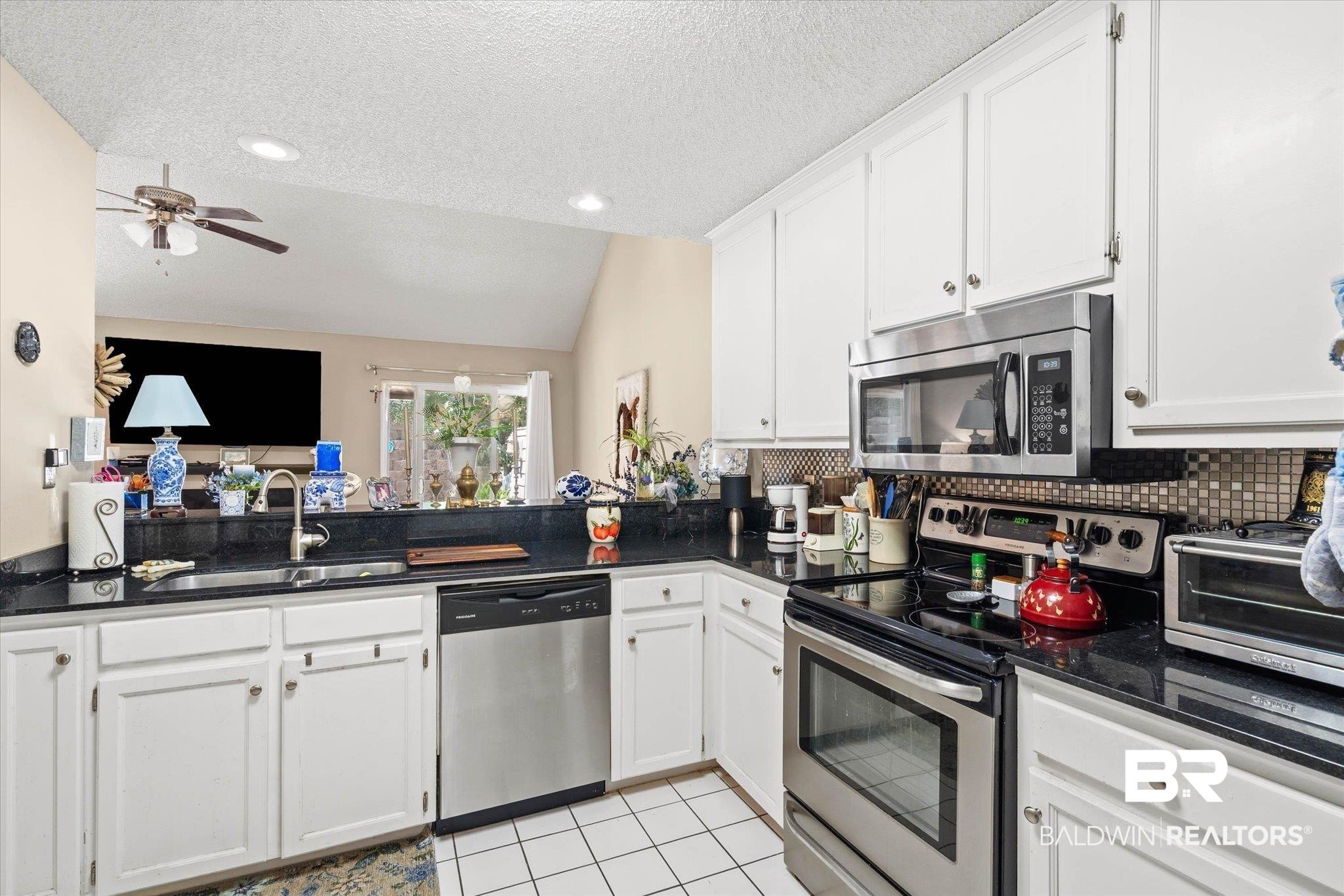Image 4: Kitchen featuring white cabinetry, black countertops, stainless steel appliances, and a mosaic tile backsplash