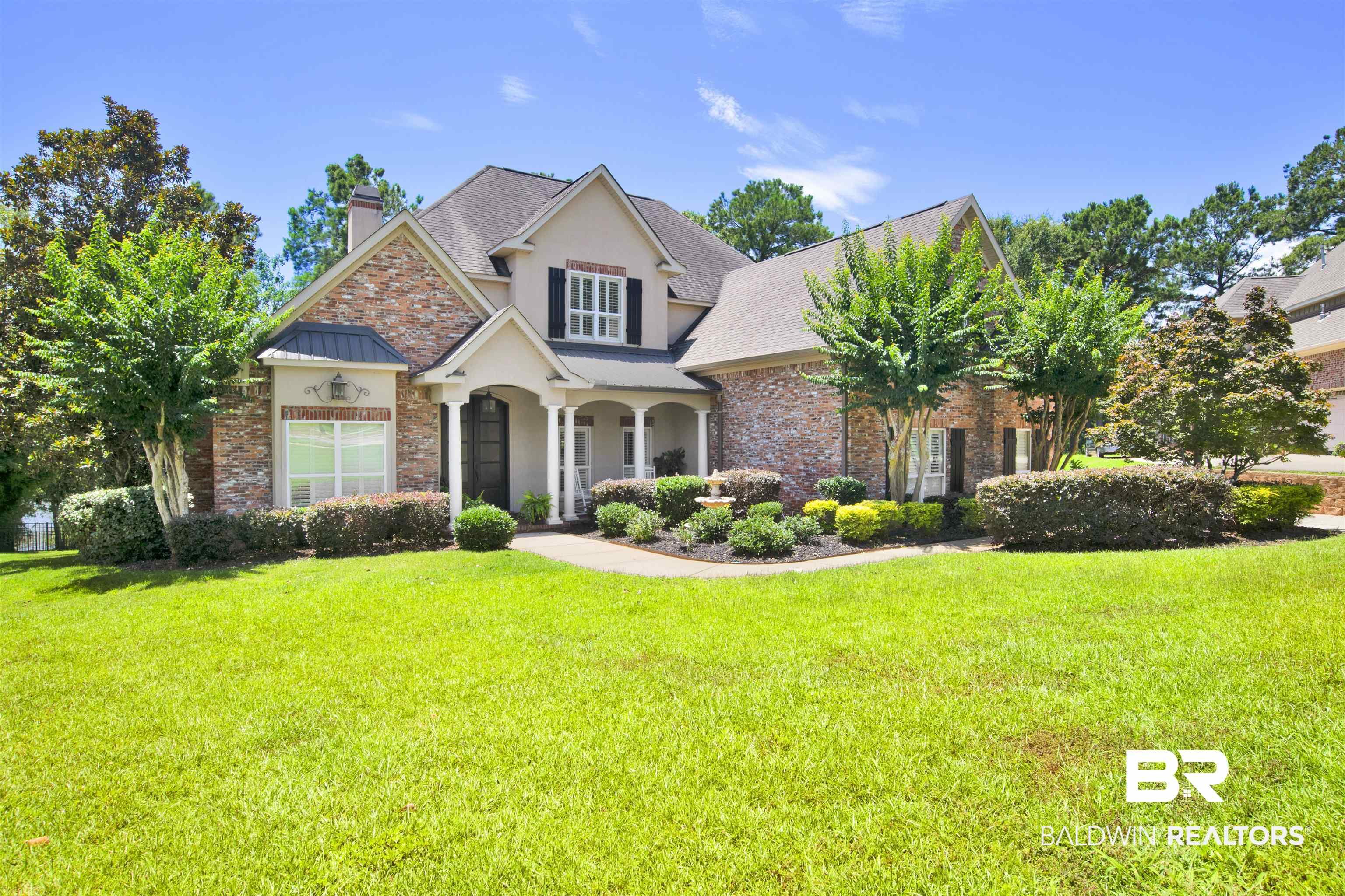 Image 2: Traditional-style residence featuring a brick and stucco exterior, a covered porch with white columns, and a dark front door with decorative glass