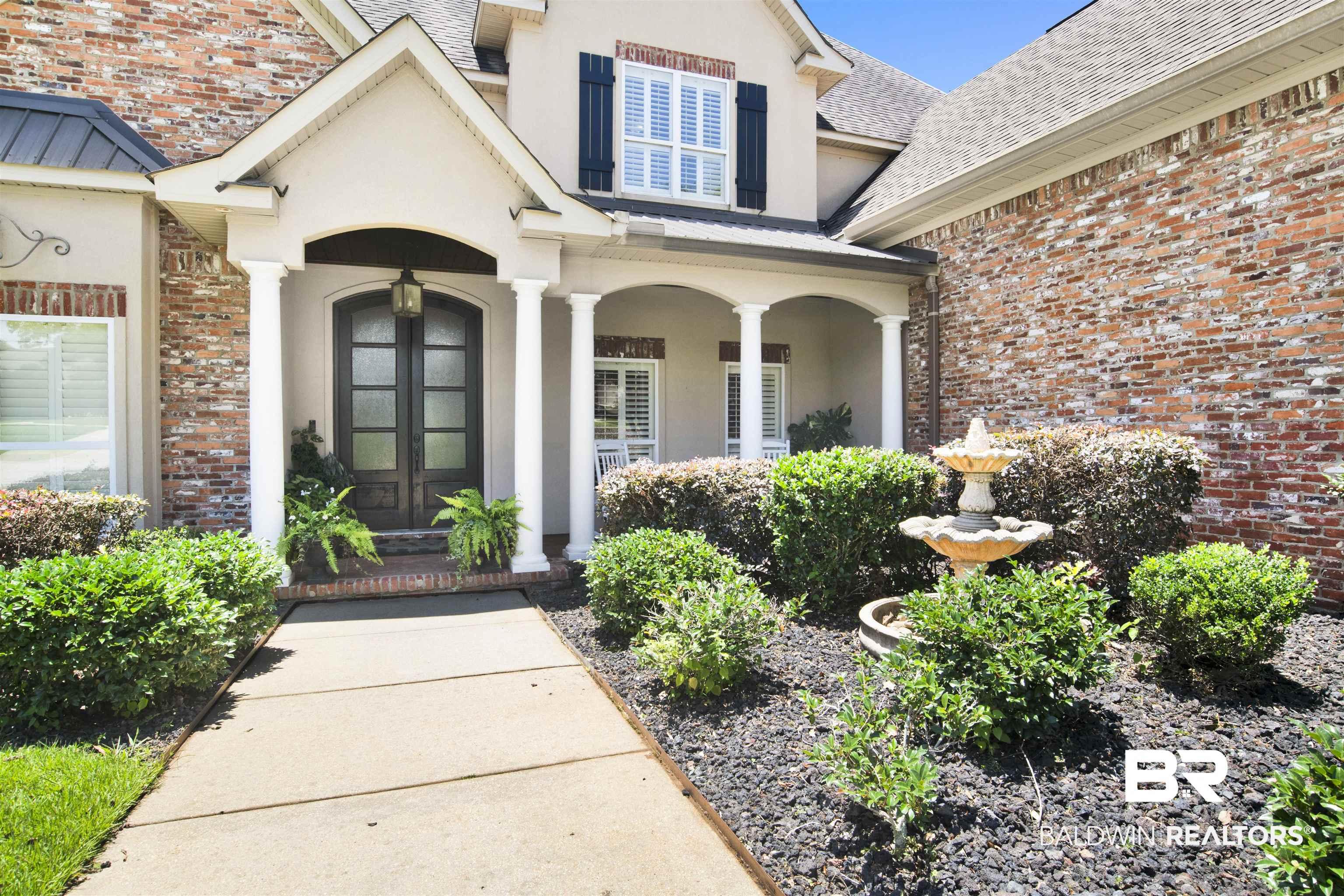 Image 3: Traditional brick and stucco exterior featuring a covered entry with columns, double-door entry with arched transom, and a tiered fountain in the landscaped front yard