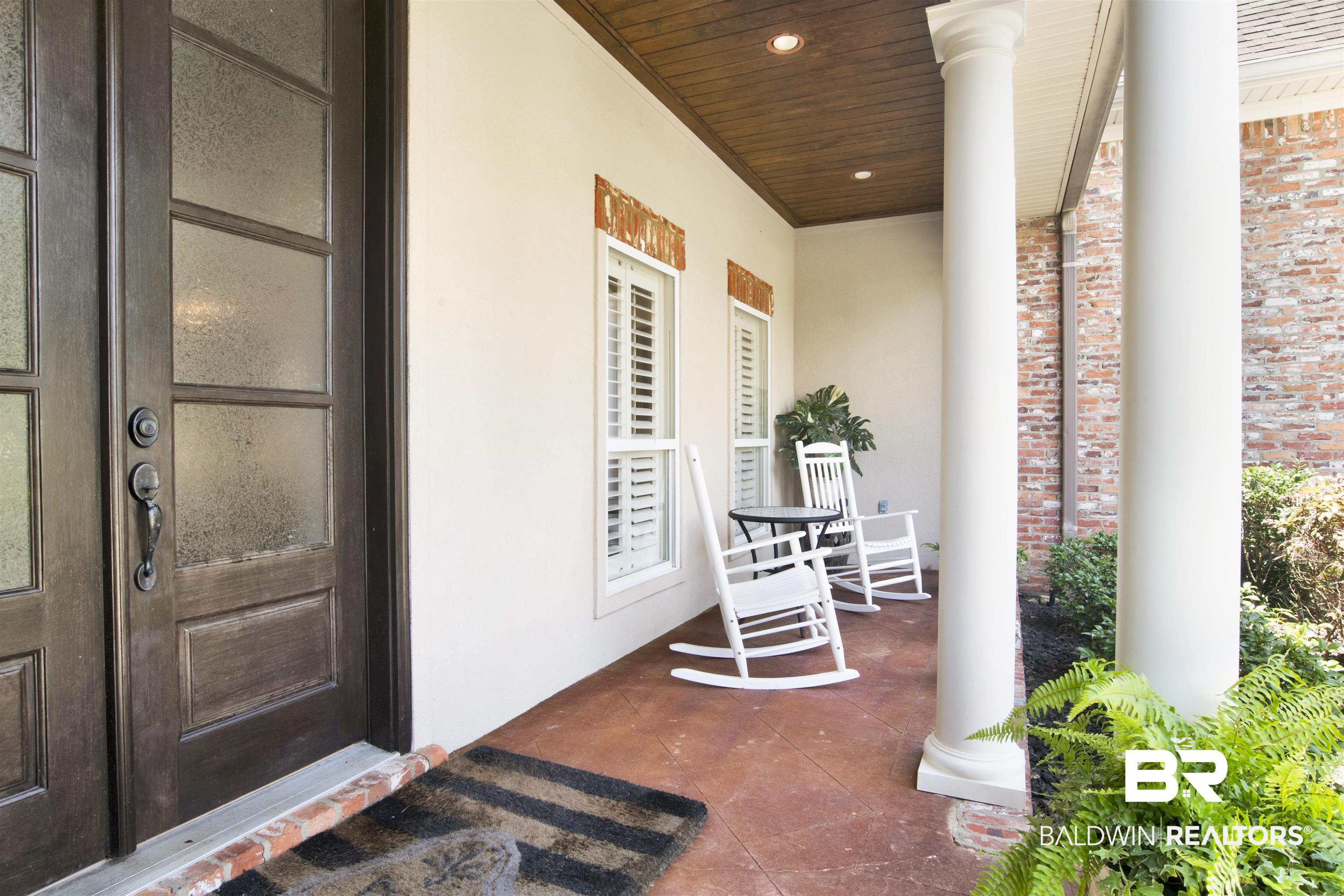 Image 4: Covered front porch featuring a dark wood entry door with multiple glass panes, white columns, and a stained concrete floor