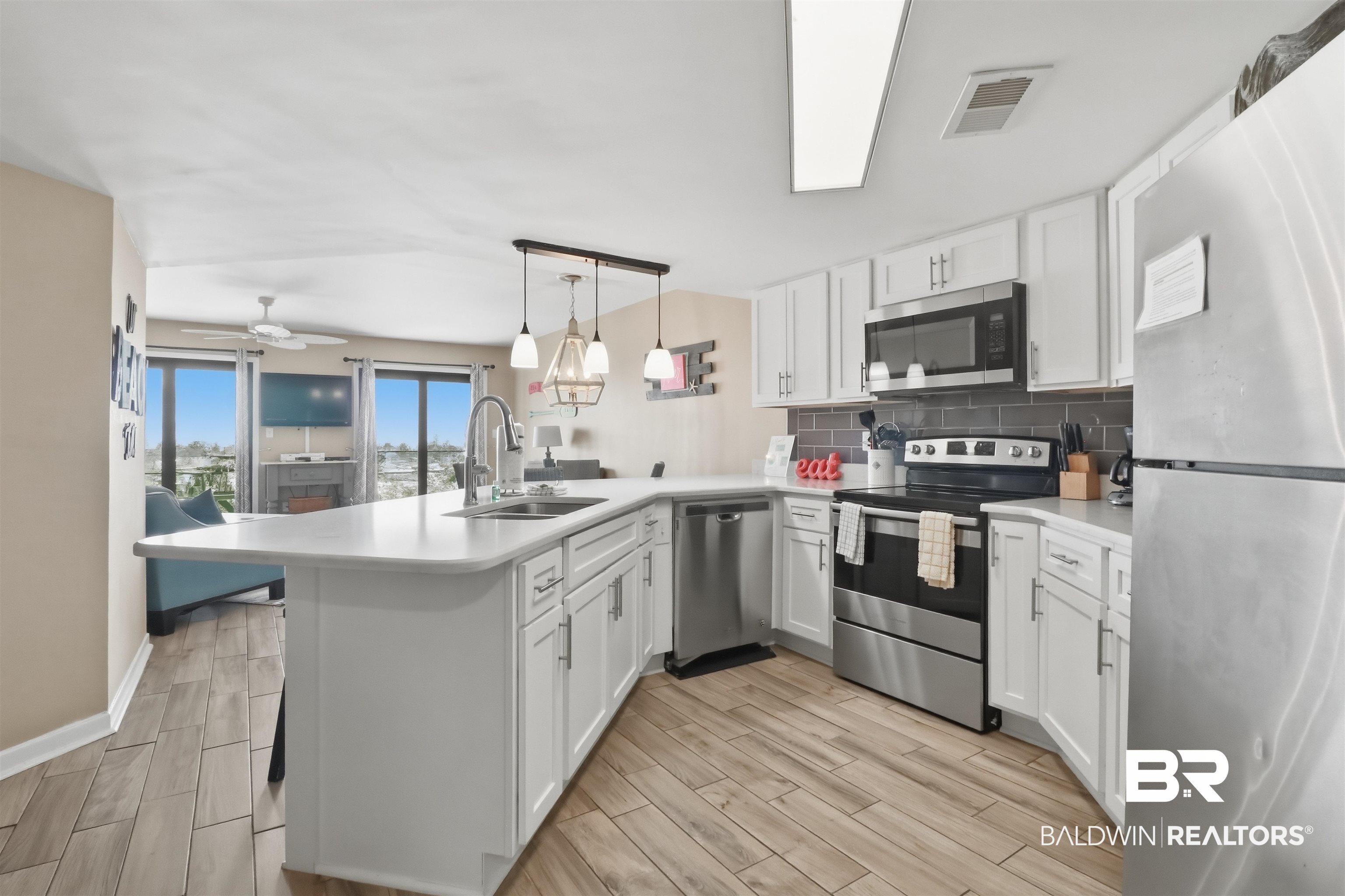Image 2: Kitchen with stainless steel appliances, light countertops, white cabinets, and tasteful backsplash