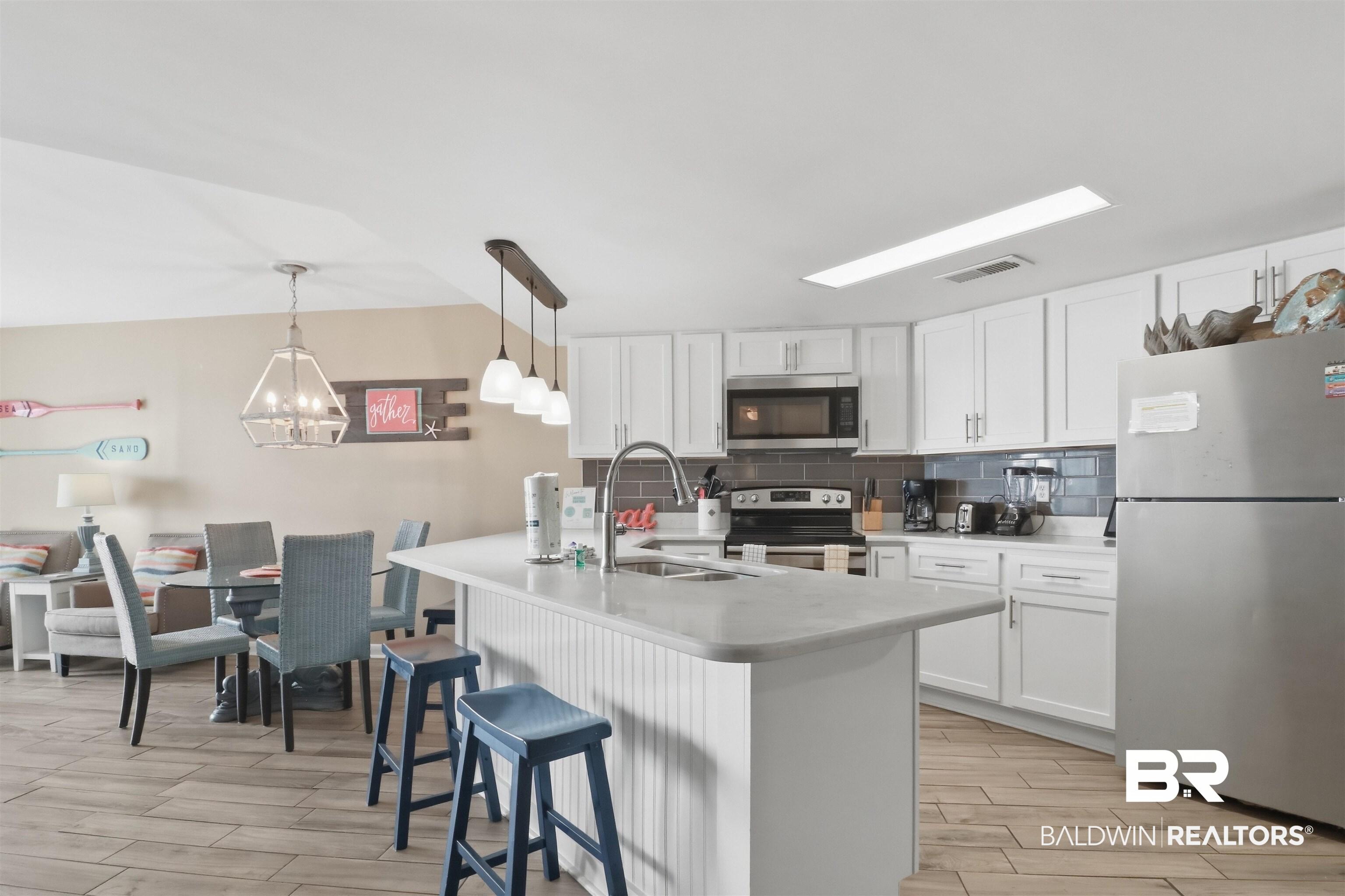 Image 3: Kitchen with stainless steel appliances, white cabinets, wood tiled floors, backsplash, and a breakfast bar area