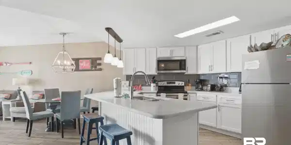 Image 3: Kitchen with stainless steel appliances, white cabinets, wood tiled floors, backsplash, and a breakfast bar area