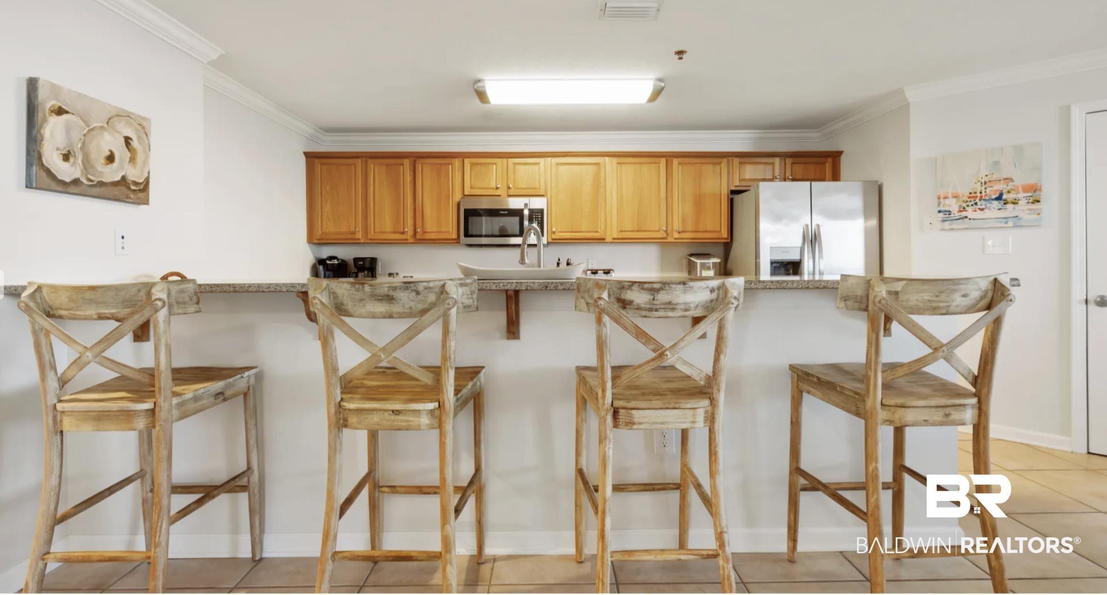 Image 4: Kitchen featuring a kitchen breakfast bar, stainless steel appliances, light tile patterned floors, wood finish cabinetry, and ornamental molding