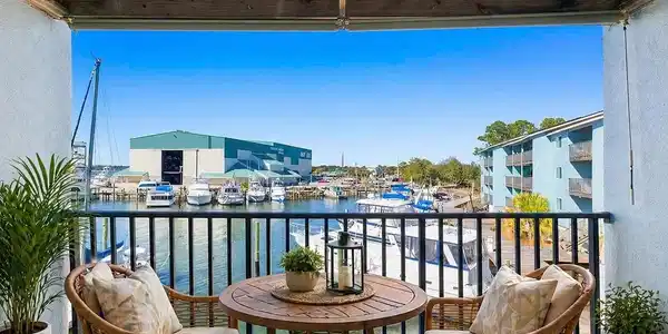 Image 2: Virtually Staged Private balcony with water frontage featuring a black wrought iron railing, wood-paneled ceiling, and a bright blue sky backdrop