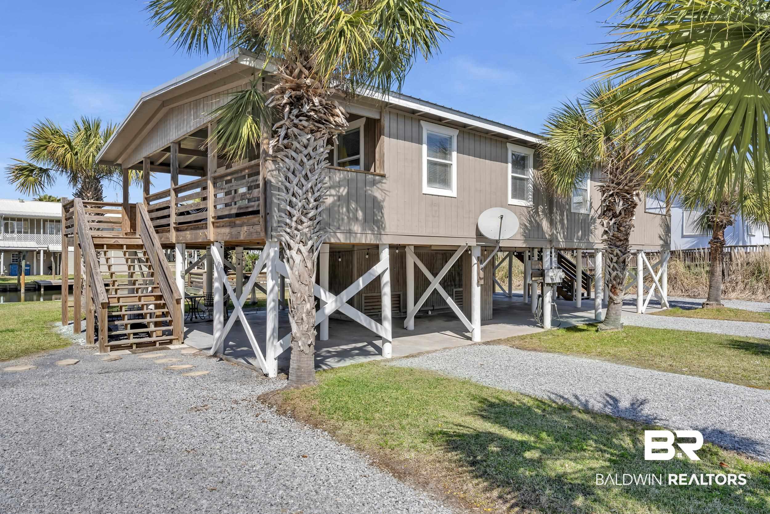 Image 2: Raised coastal-style home featuring a covered porch with wood railing, exterior stairs, and gravel driveway