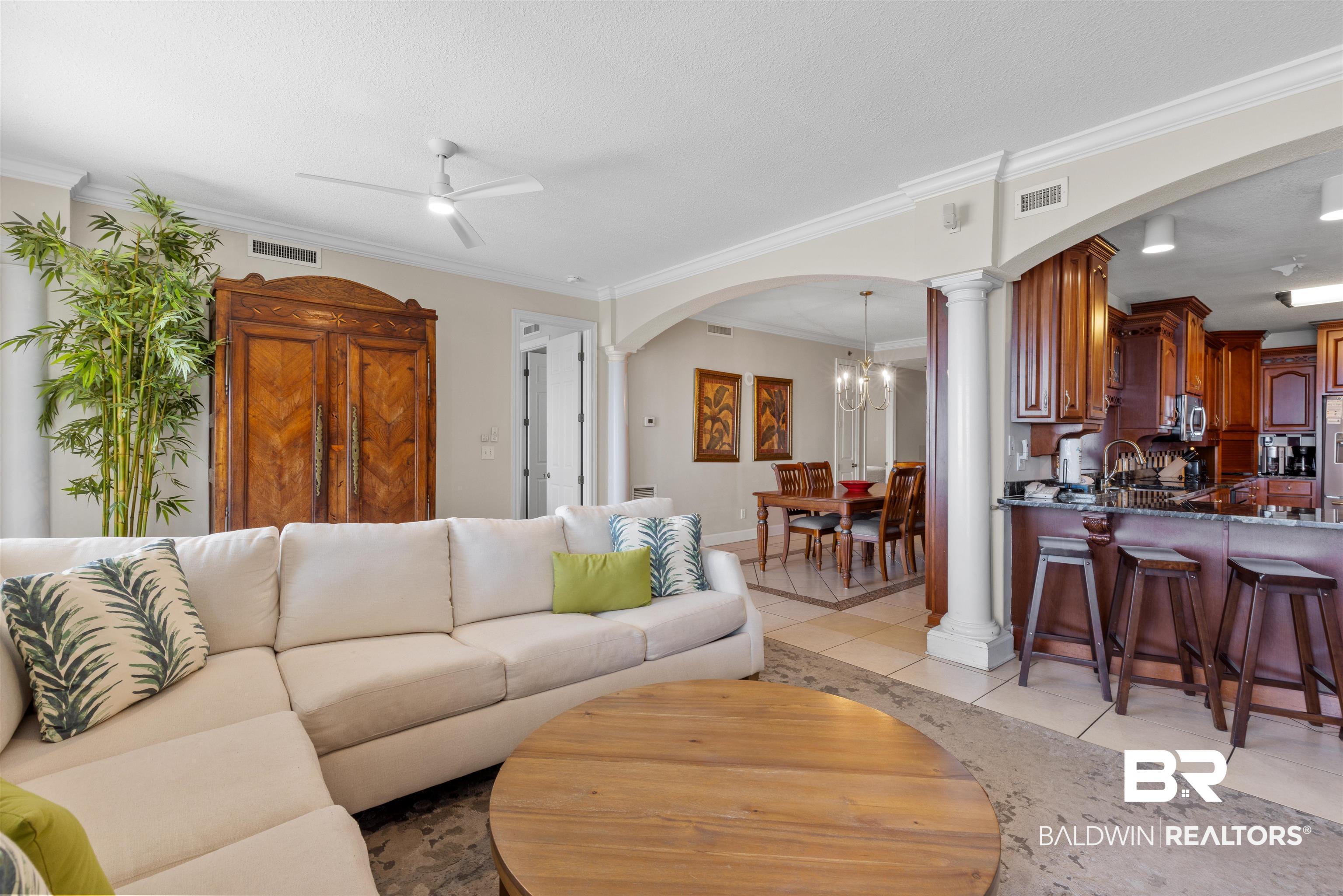 Image 4: Living room with crown molding, light tile patterned flooring, a chandelier, ceiling fan, and ornate columns