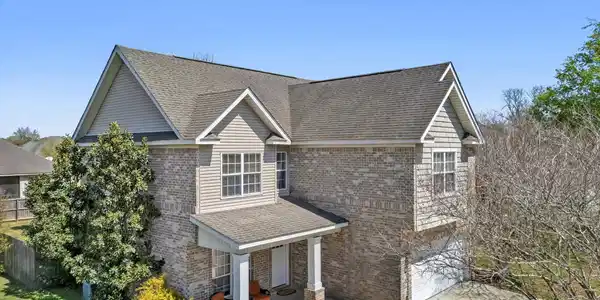 Image 2: View of front of property with brick siding, covered porch, a garage, and roof with shingles