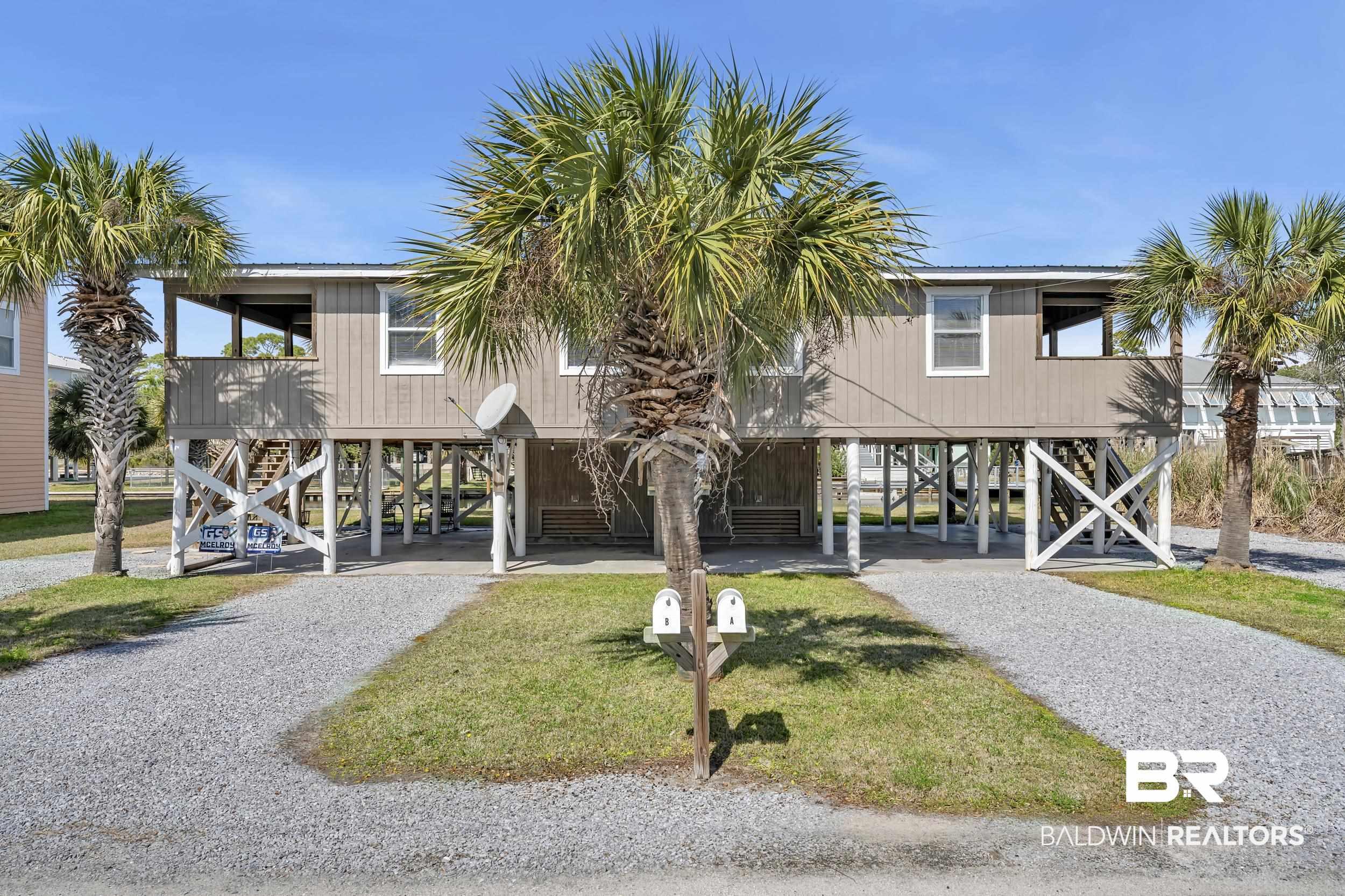 Image 4: Stilt-raised duplex featuring two separate gravel driveways, multiple mature palm trees, and a covered upper-level porch