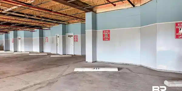 Image 2: Concrete parking structure with exposed ceiling joists and utility pipes