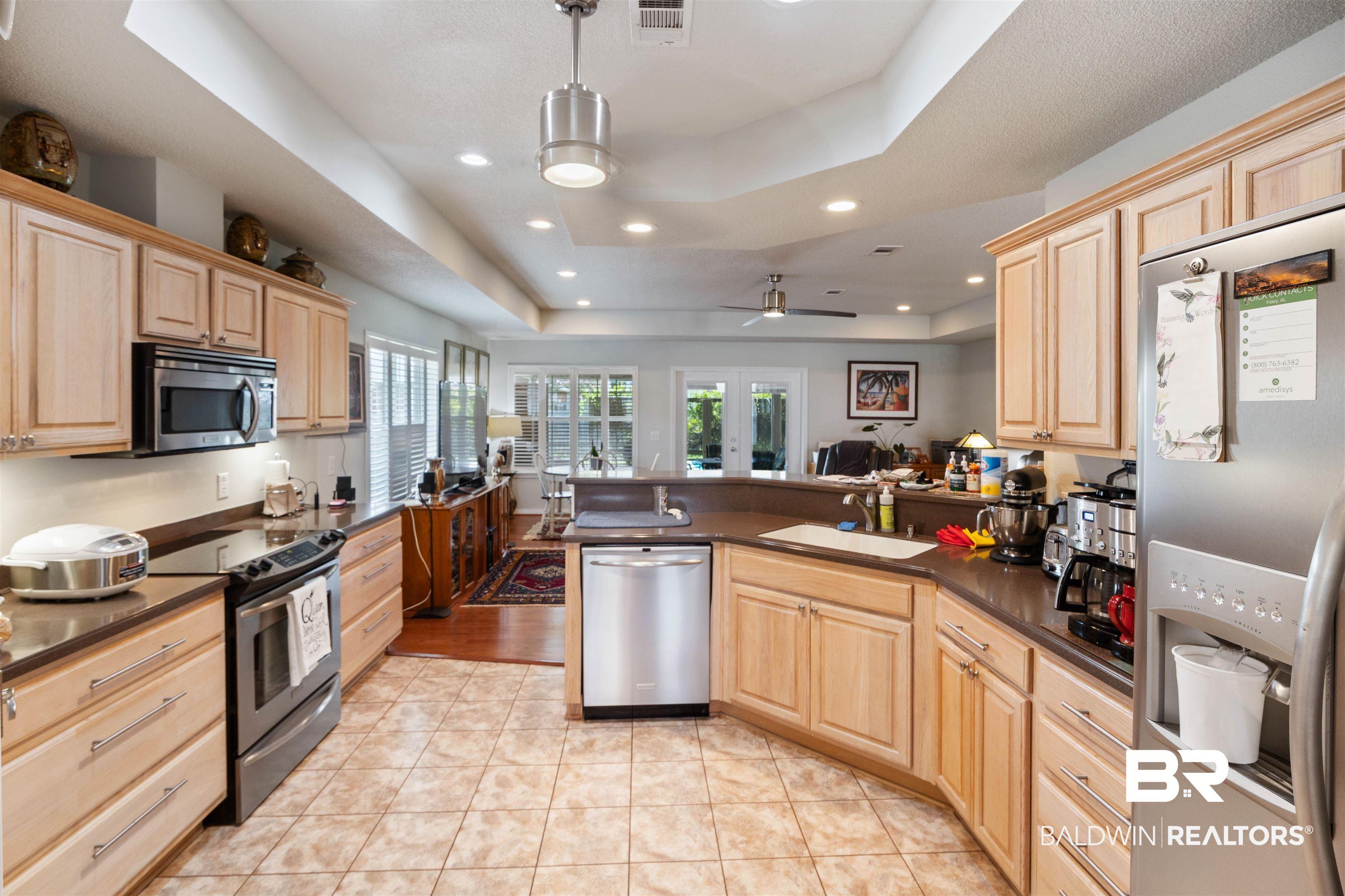 Image 4: Spacious kitchen featuring light wood cabinetry, dark countertops, a stainless steel appliance suite, recessed lighting, and tile flooring