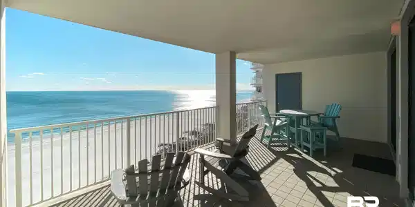 Image 3: Spacious covered balcony with tile flooring, white railing, and panoramic ocean and beach scenery