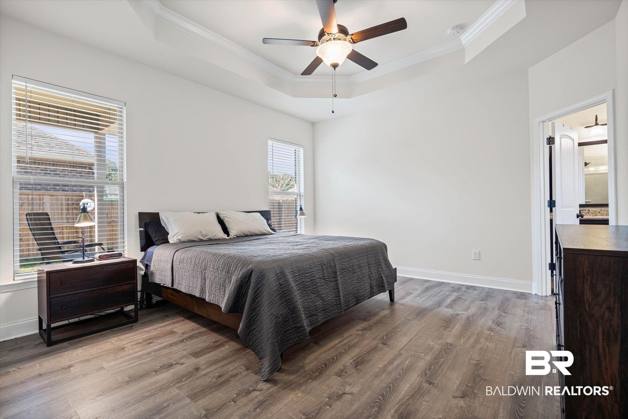 Image 4: Bedroom with ornamental molding, light wood finished floors, a ceiling fan, and a tray ceiling