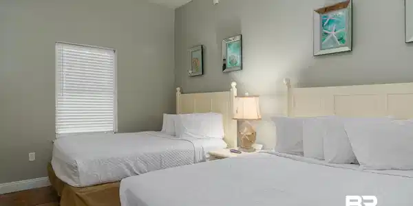 Image 2: Room featuring two beds with white headboards, a window with blinds, wood-finish flooring, and light grey walls