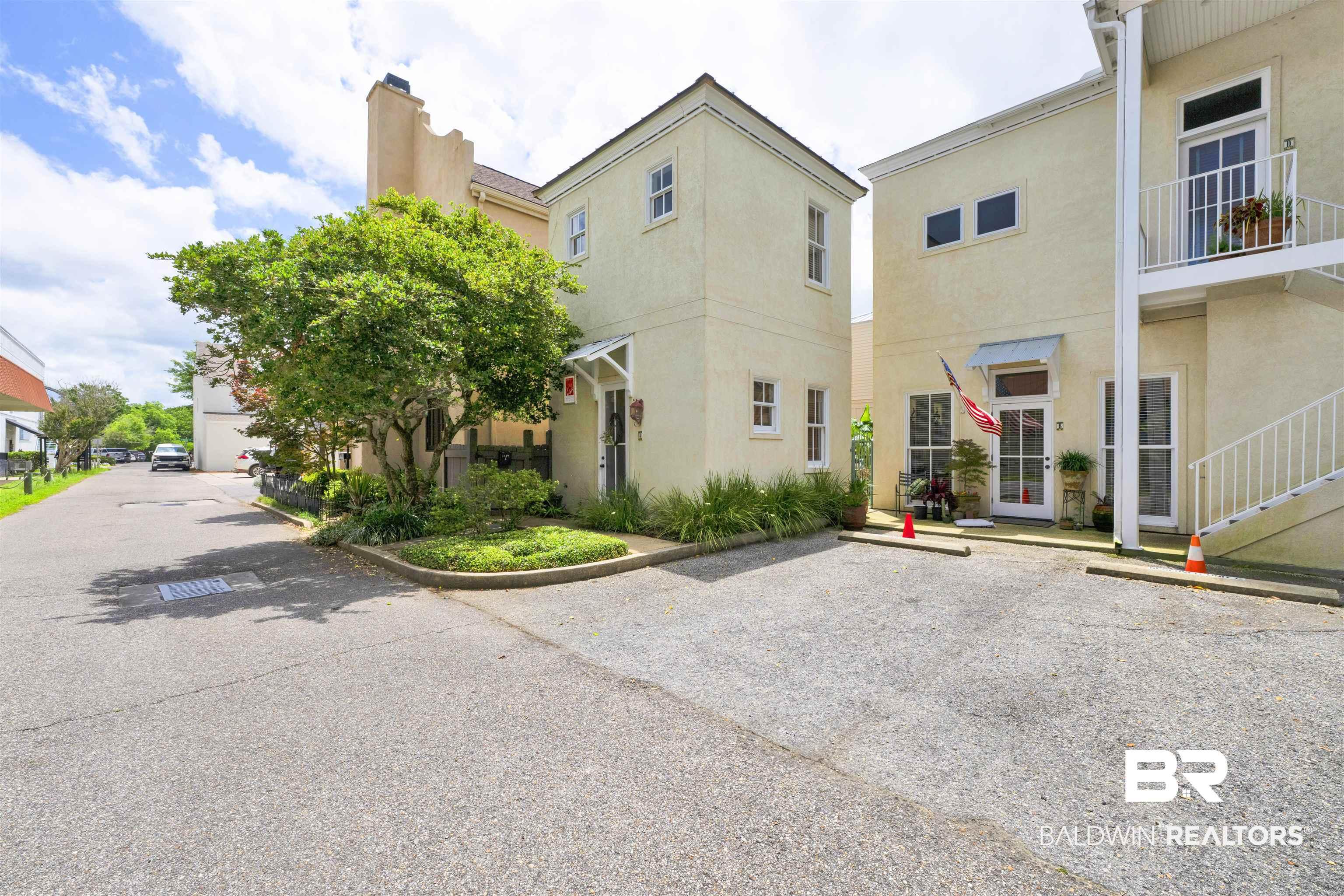 Image 1: Cream stucco exterior with white trim, featuring a prominent mature tree and landscaping beds