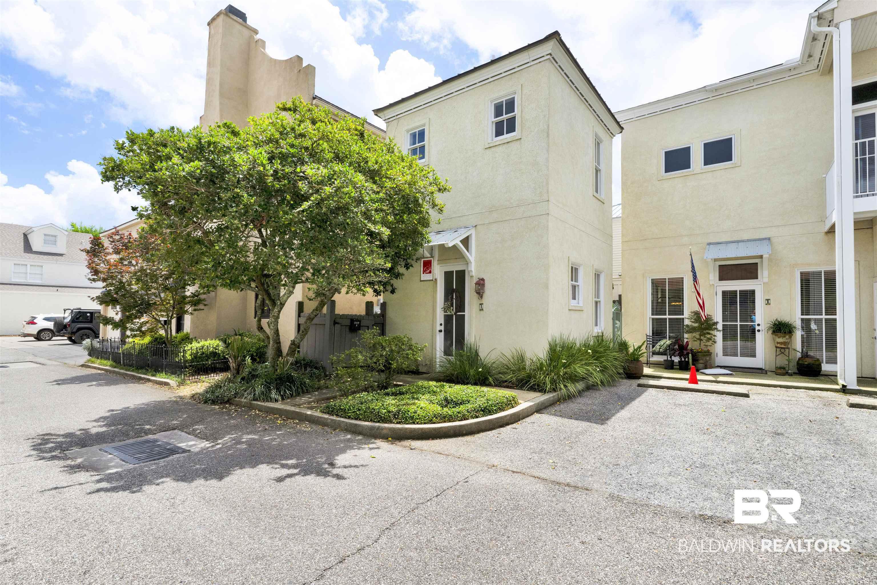 Image 2: Stucco exterior featuring white-framed windows, a covered entry with a decorative awning, and mature trees providing natural shading