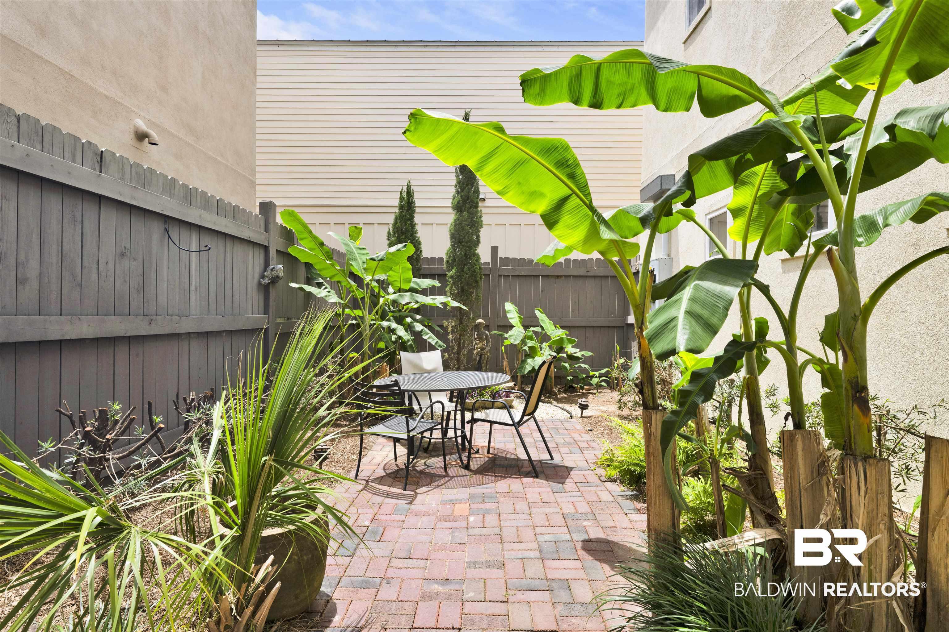 Image 4: Private outdoor patio featuring a brick paver surface, mature tropical plantings, and a privacy fence