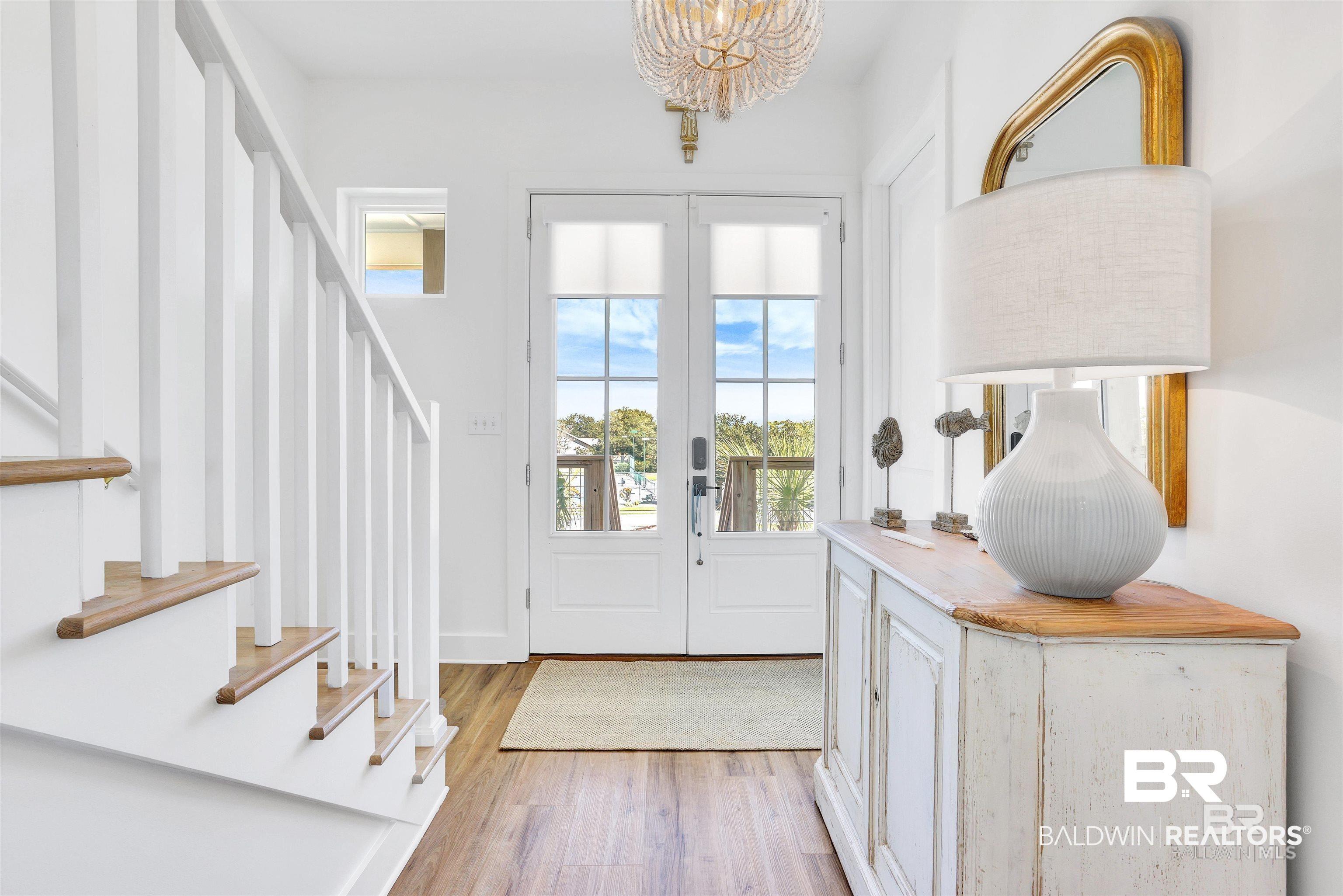 Image 3: Entryway featuring wood-finish flooring, a white staircase with wood treads, and white French doors with upper window panes