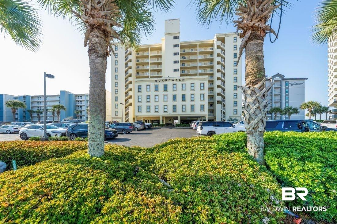 Image 2: Multi-story building featuring an exterior parking area, multiple balconies, and ground-level landscaping with mature palm trees