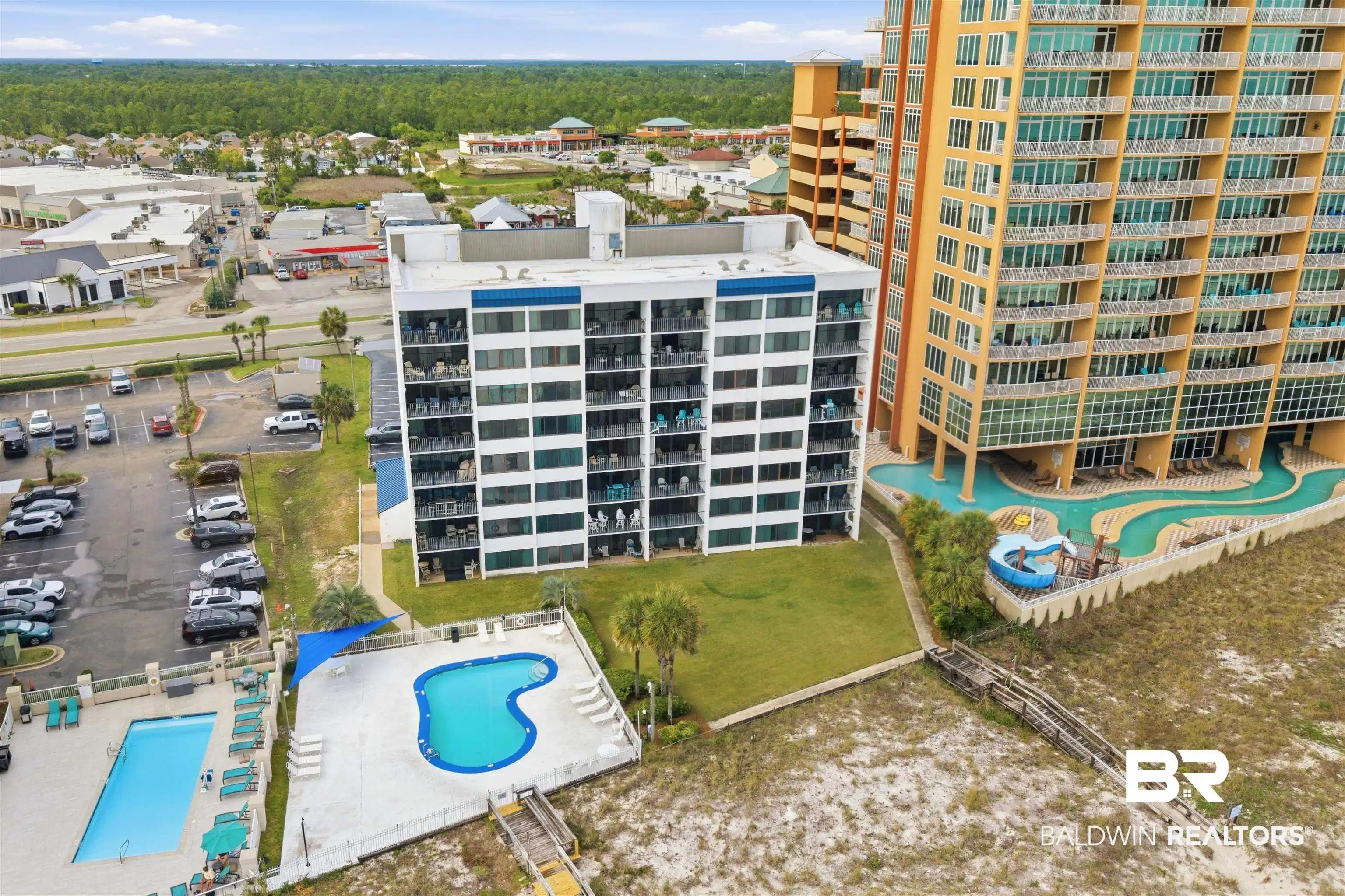 Image 1: Coastal high-rise property featuring multiple swimming pools, a wooden boardwalk, and surrounding green spaces