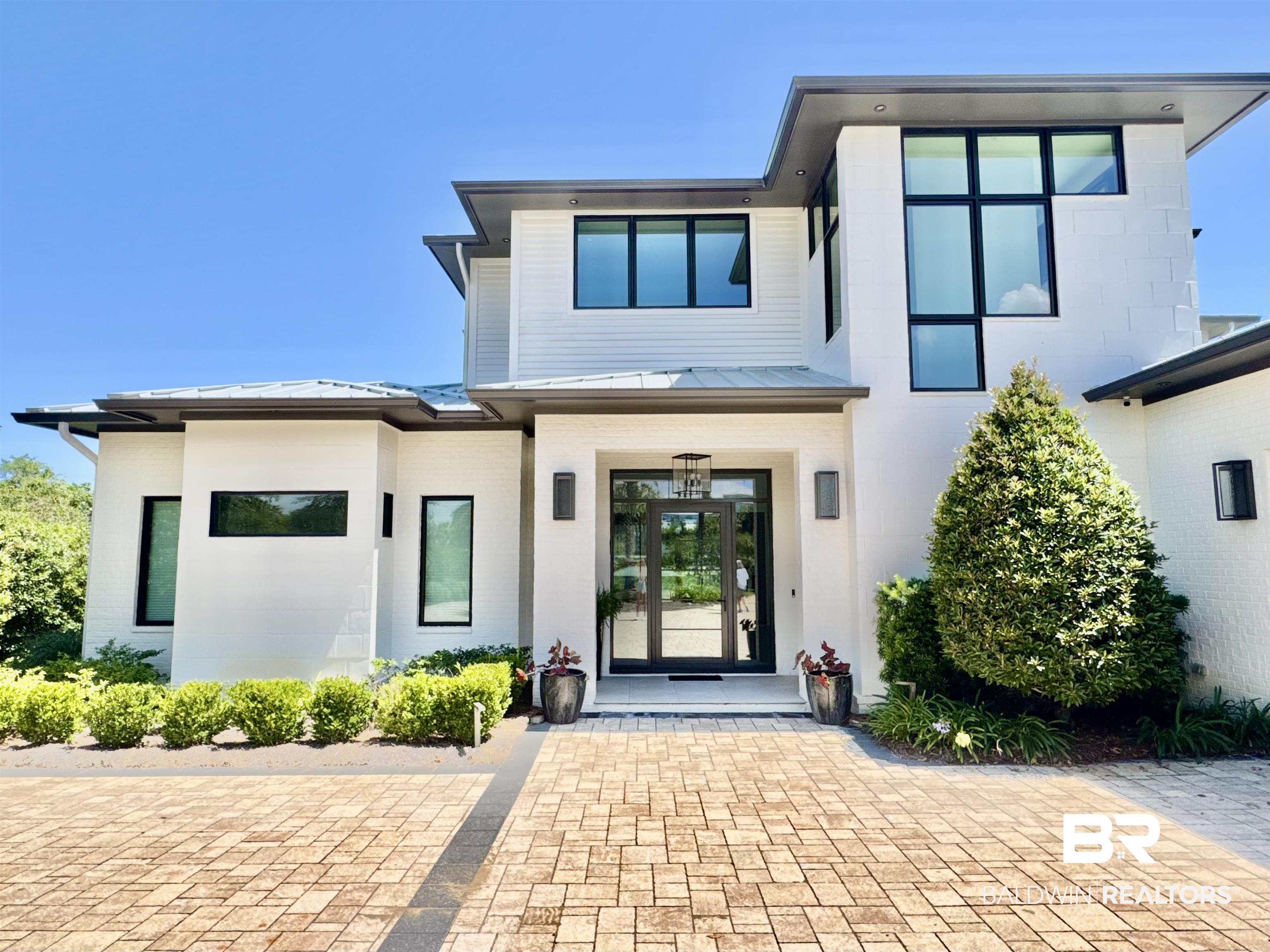 Image 4: Contemporary exterior featuring white brick and horizontal siding, black-framed windows, a glass-paneled entry door, a paver driveway, and manicured landscaping