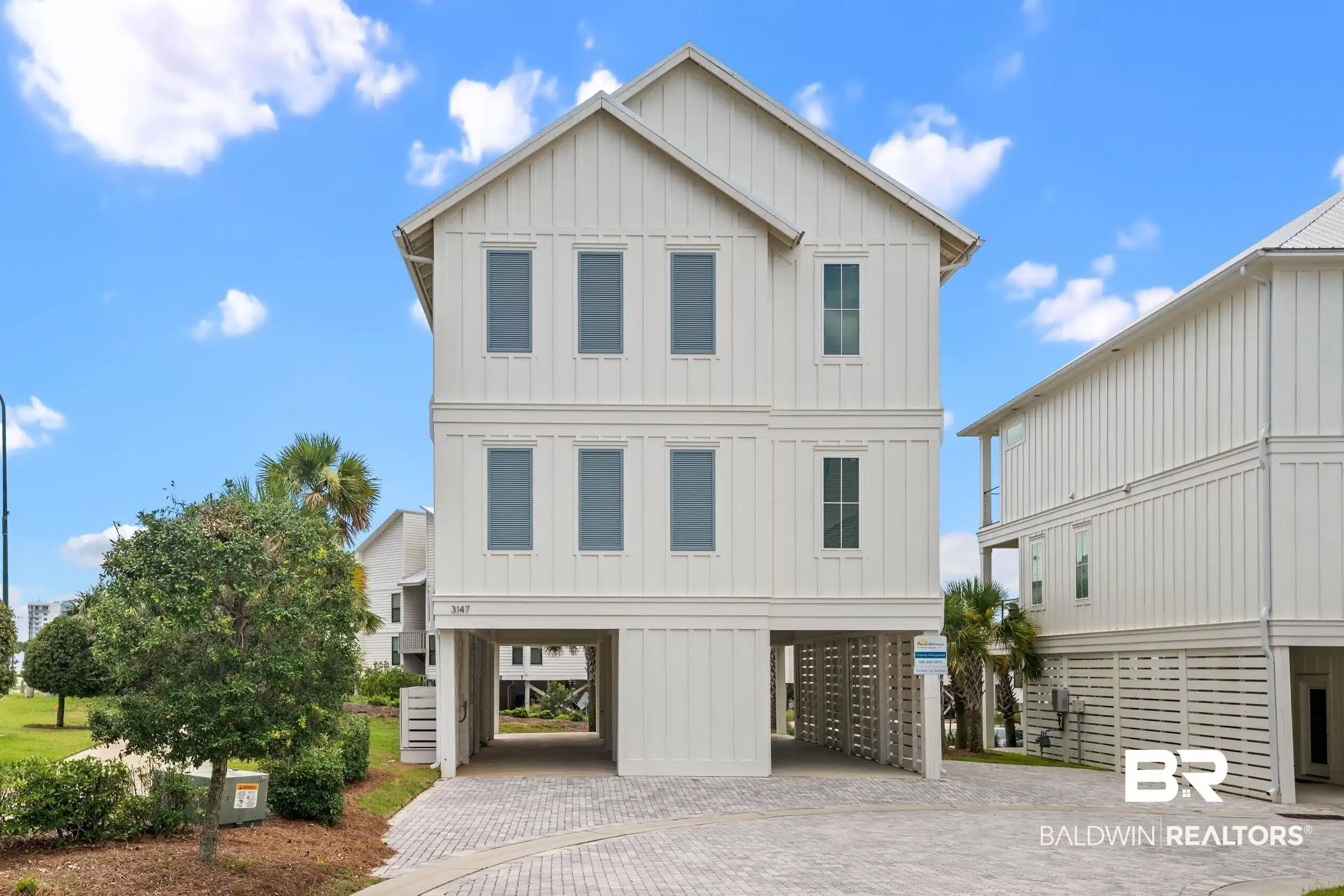 Image 1: Coastal inspired home with board and batten siding, a carport, and decorative driveway