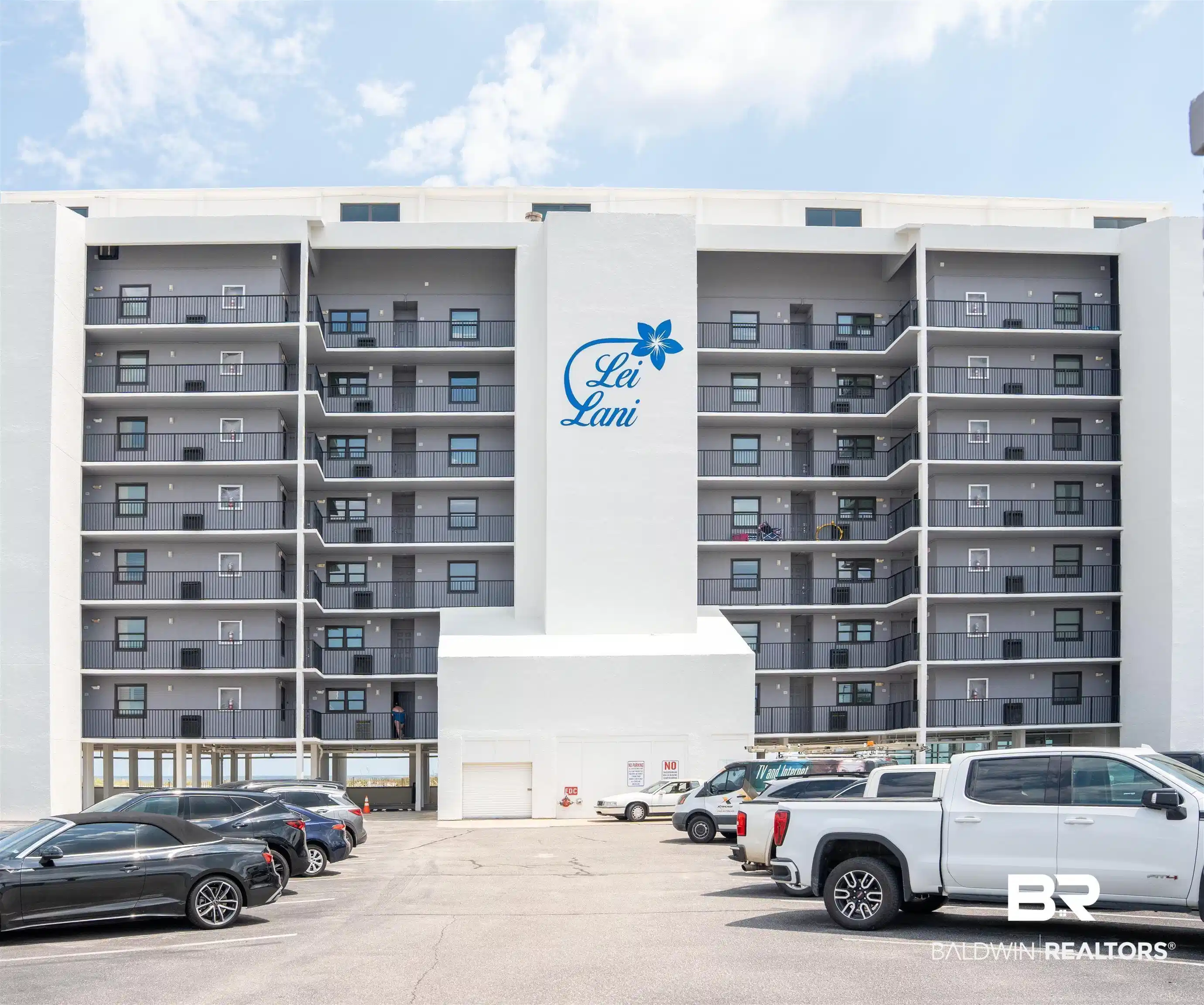 Image 1: Multi-story building featuring stacked balconies with dark railings, a prominent central white facade with "Lei Lani" branding, and a ground-level parking area