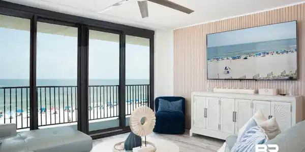 Image 3: Expansive sliding glass doors open to a balcony with black metal railings, overlooking a sandy beach and ocean