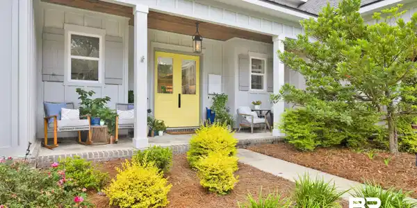 Image 2: Inviting front porch featuring a vibrant yellow double-door entry, board and batten siding, substantial white columns, and natural wood-finish porch ceilings