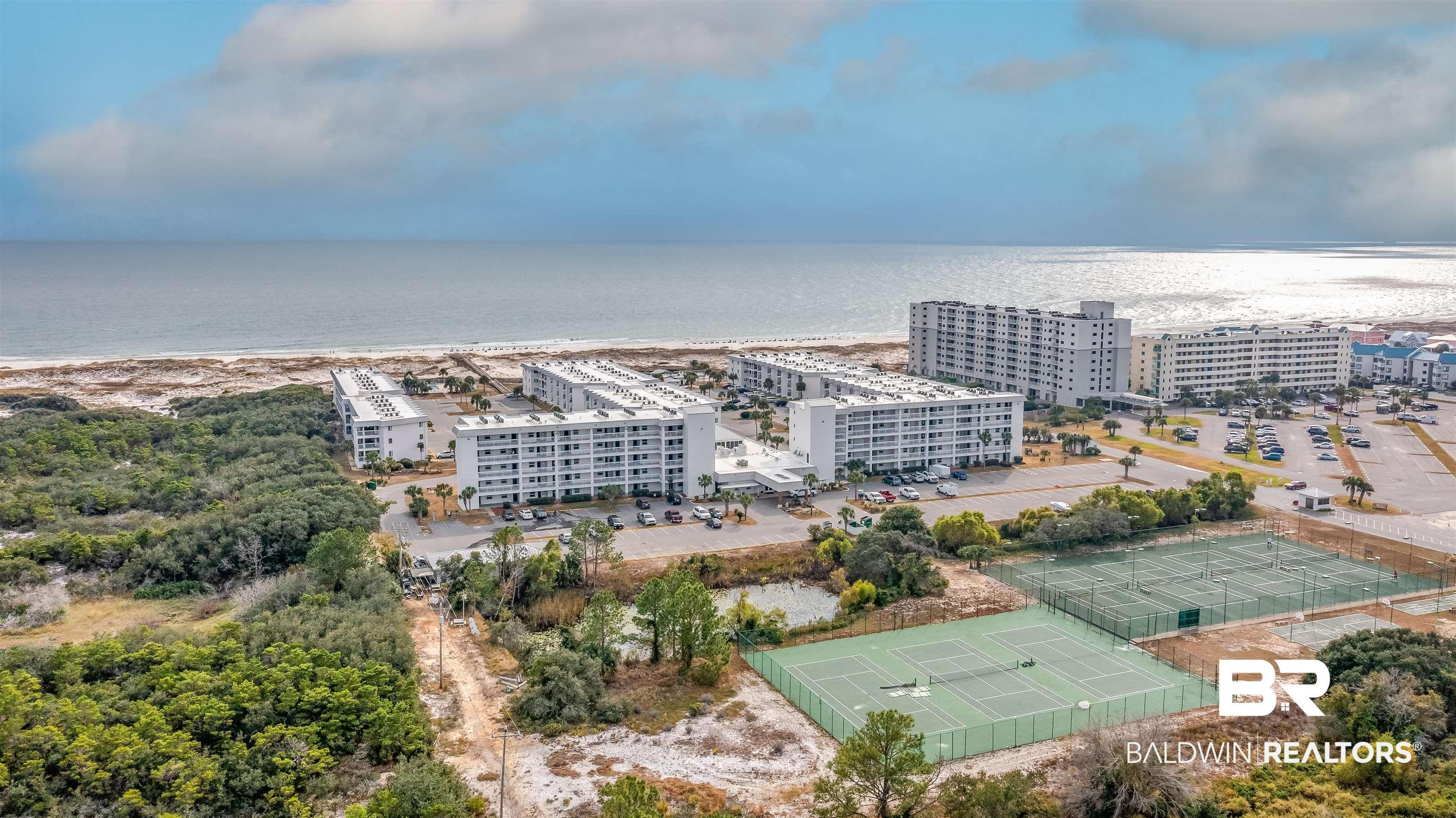 Image 1: Coastal residential complex featuring multiple buildings with balconies, extensive parking areas, and several fenced tennis courts