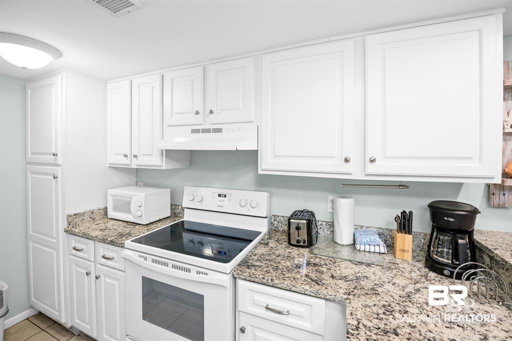 Image 2: Kitchen with white appliances, white cabinets, under cabinet range hood, and light stone counters