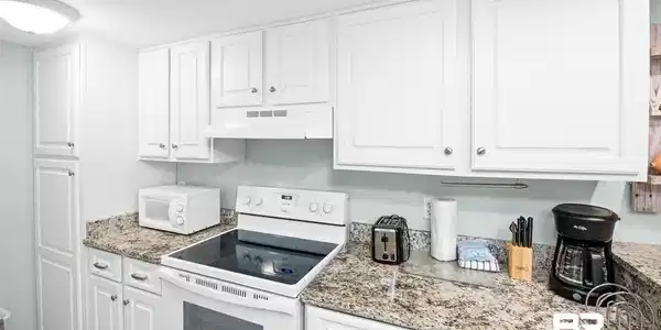 Image 2: Kitchen with white appliances, white cabinets, under cabinet range hood, and light stone counters