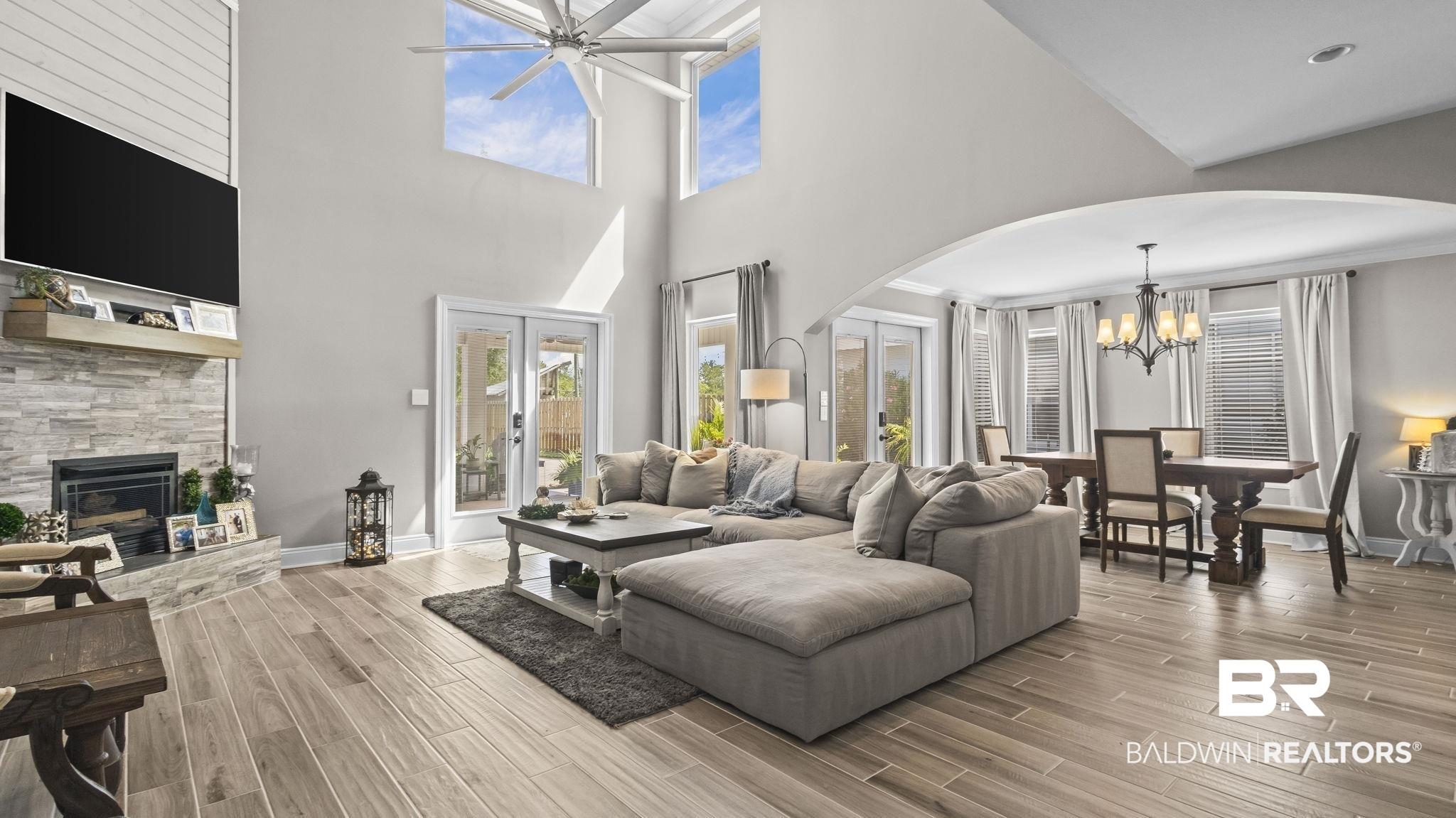 Image 4: Living room featuring arched walkways, a chandelier, ceiling fan, a stone fireplace, and plenty of natural light