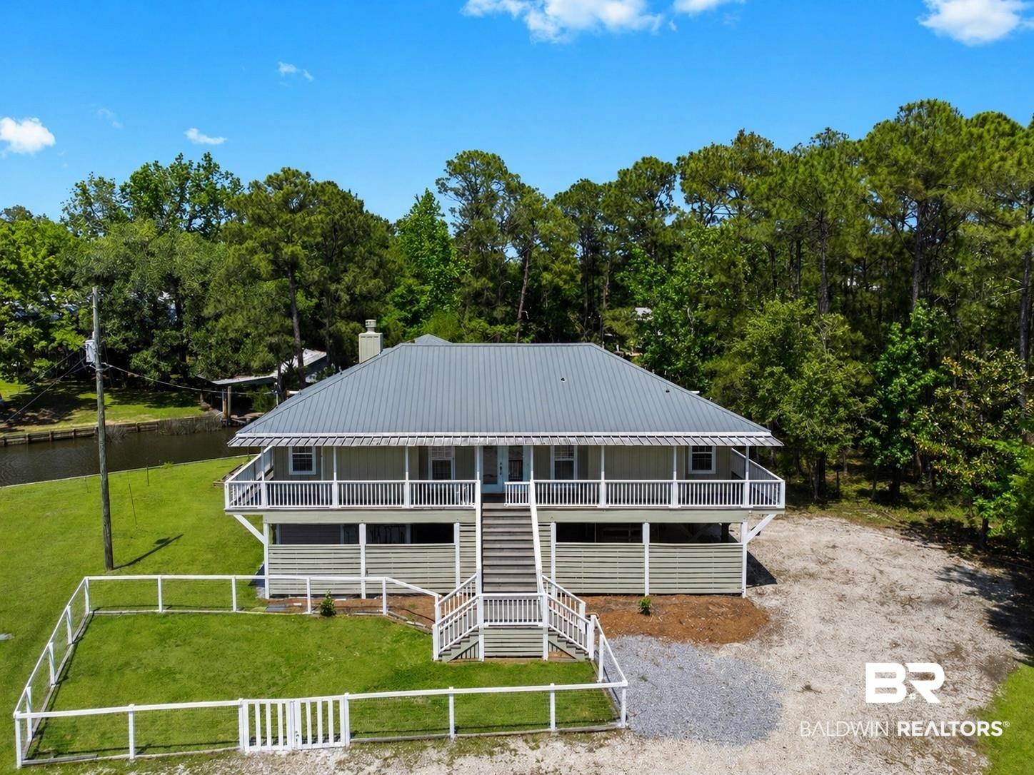 Image 1: Elevated residence featuring a grey metal roof, wrap-around porch, and a fenced grassy area