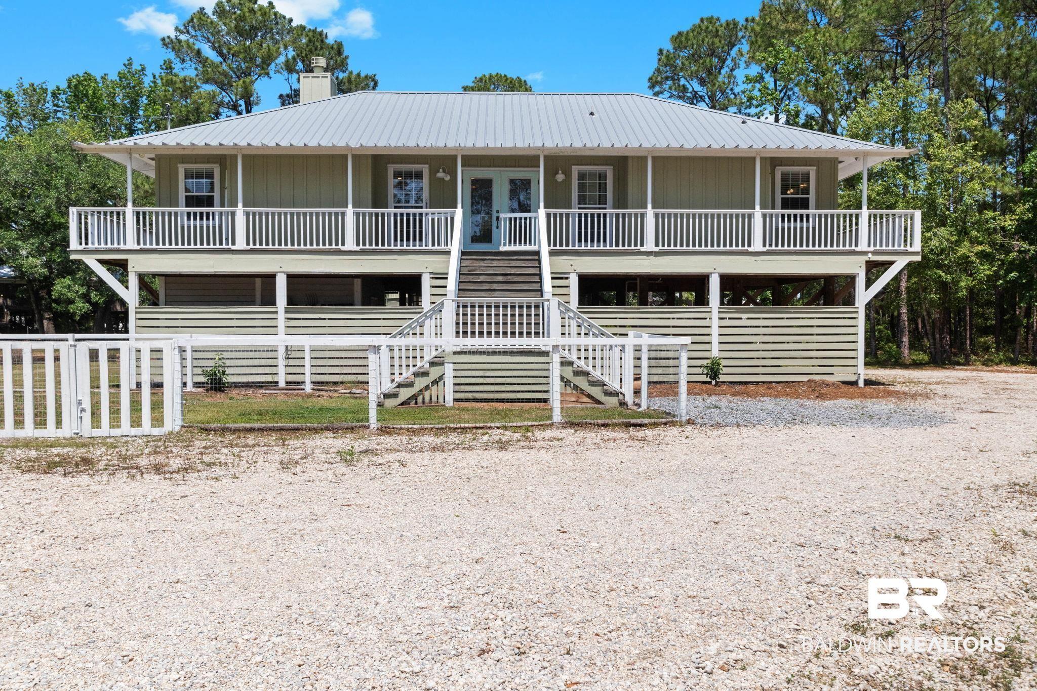 Image 4: Elevated residence featuring a metal roof, a full-width covered porch with white railings, and light green horizontal siding