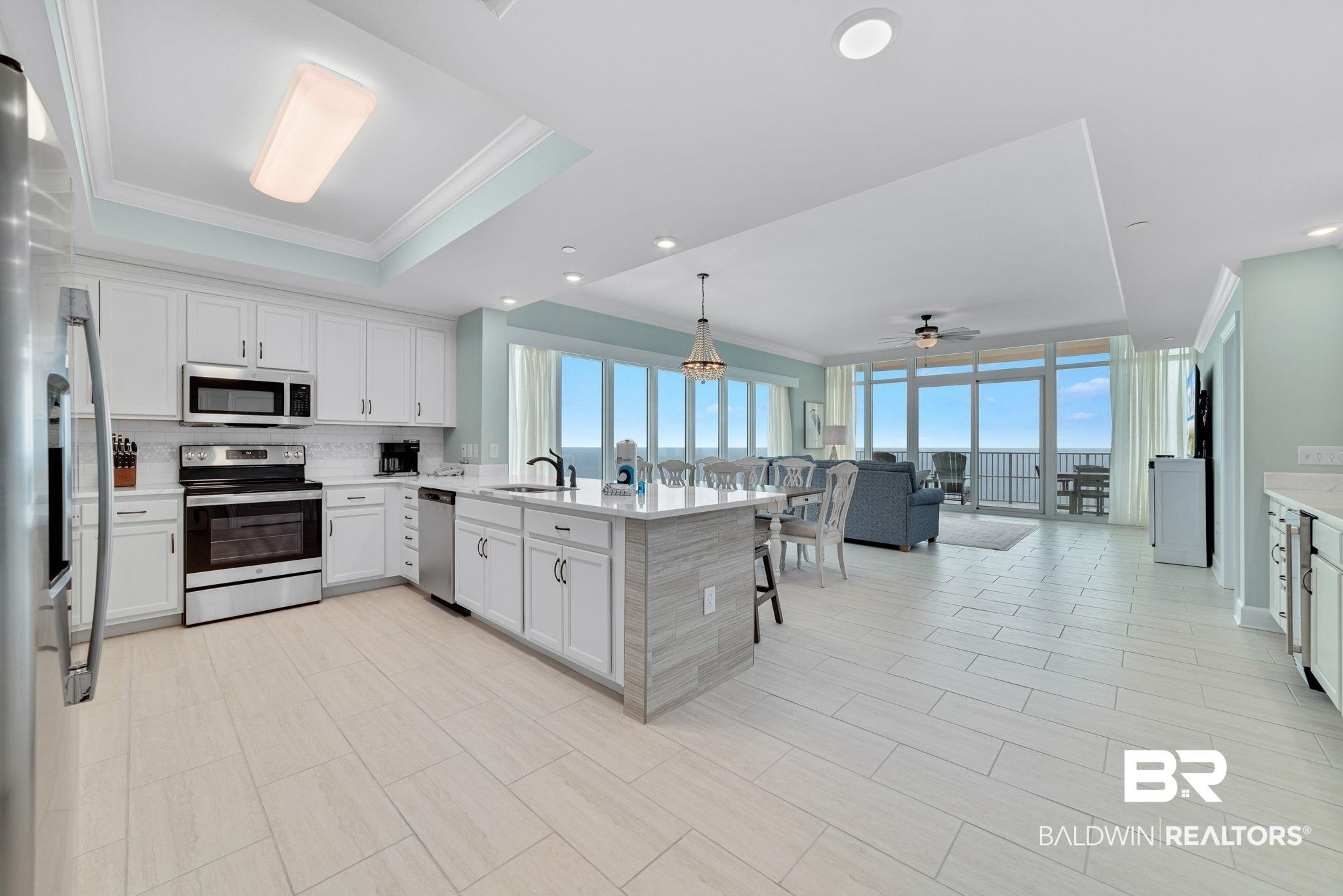 Image 2: Open-concept living space with a contemporary kitchen featuring white cabinetry, stainless steel appliances, and a central island with a sink