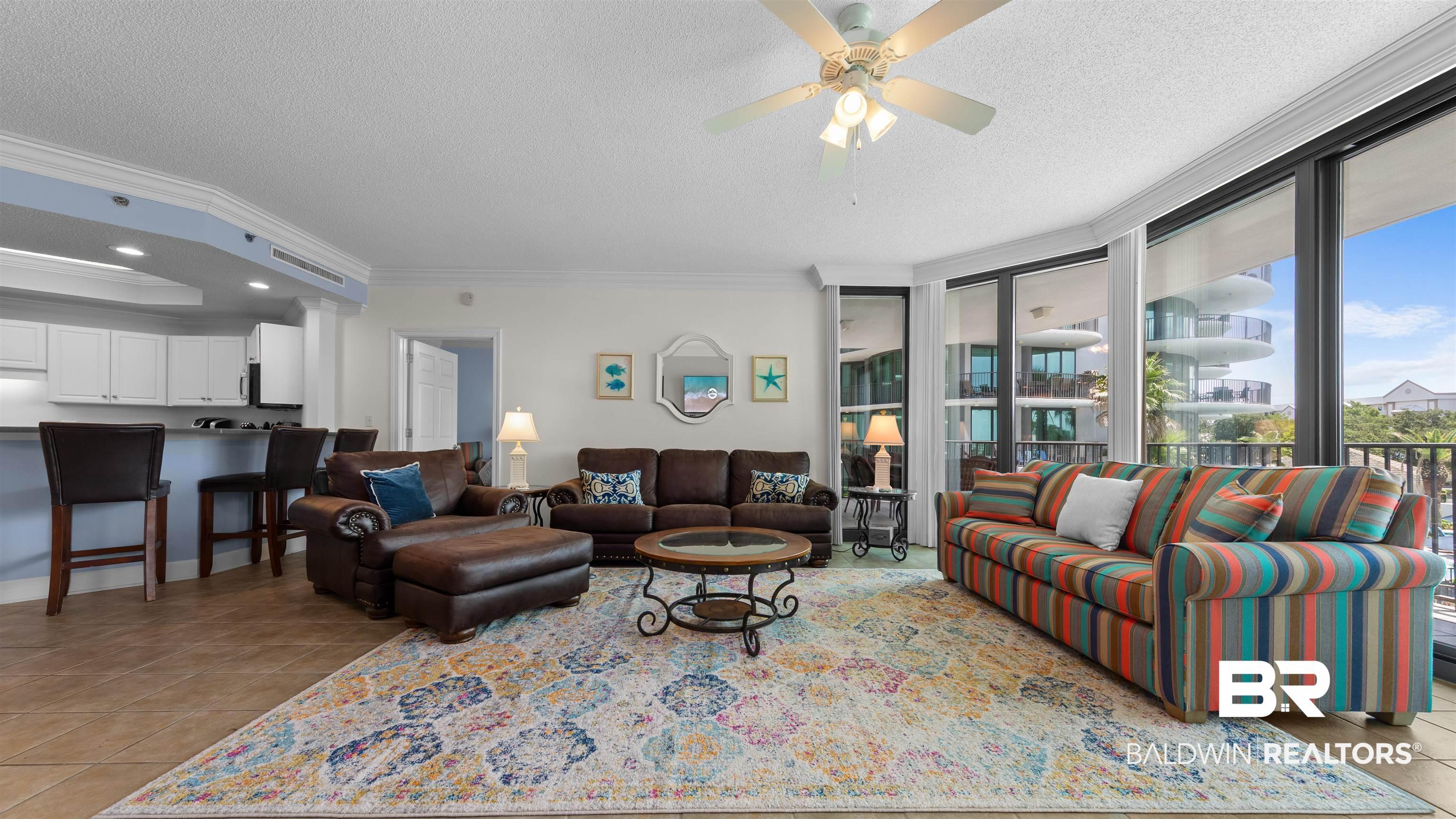 Image 2: Living area with ornamental molding, light tile patterned flooring, a textured ceiling, a ceiling fan, and a raised ceiling