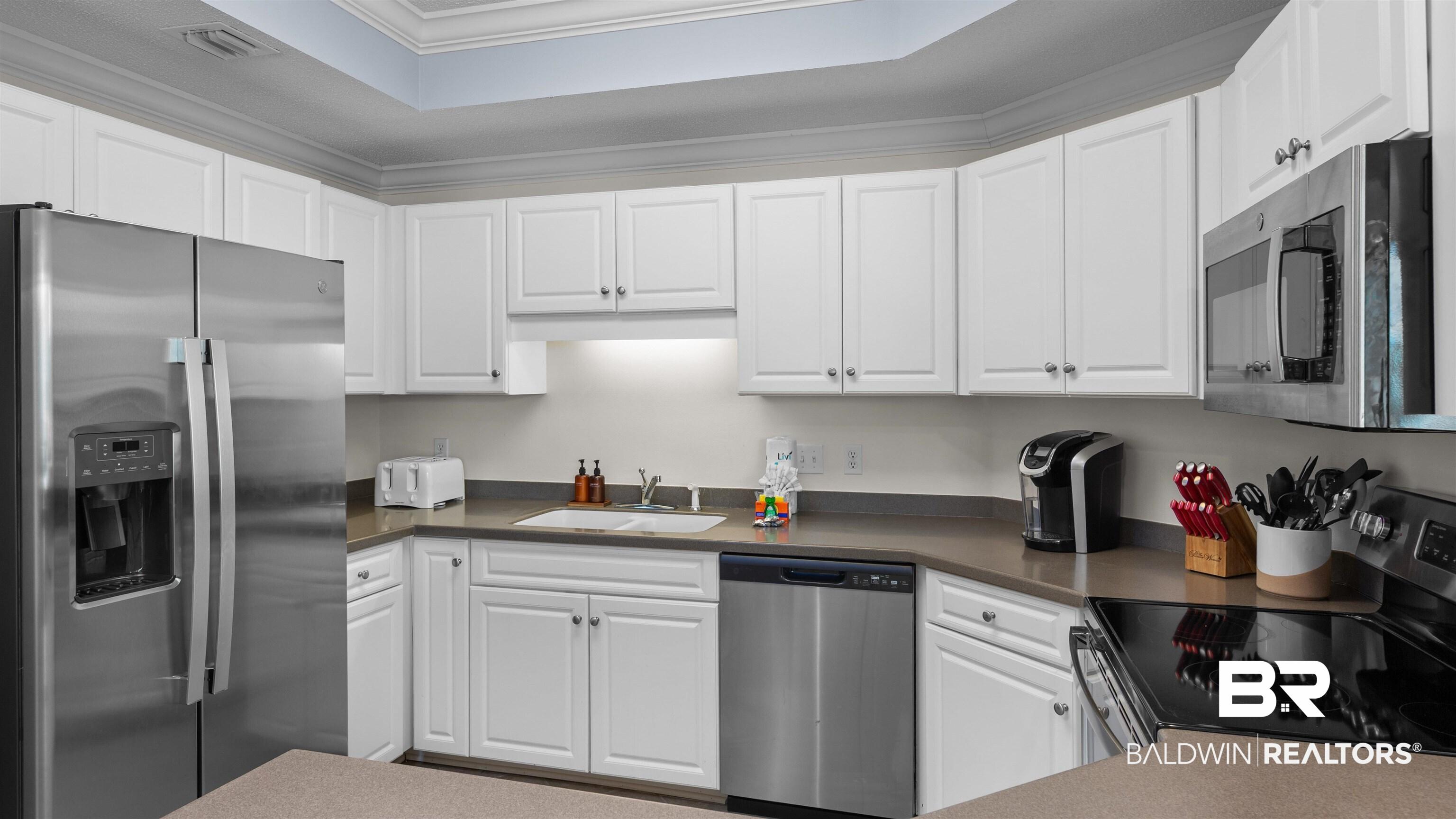 Image 3: Kitchen with stainless steel appliances, white cabinets, crown molding, a raised ceiling, and dark countertops