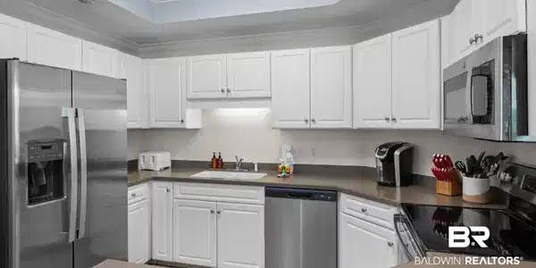 Image 3: Kitchen with stainless steel appliances, white cabinets, crown molding, a raised ceiling, and dark countertops