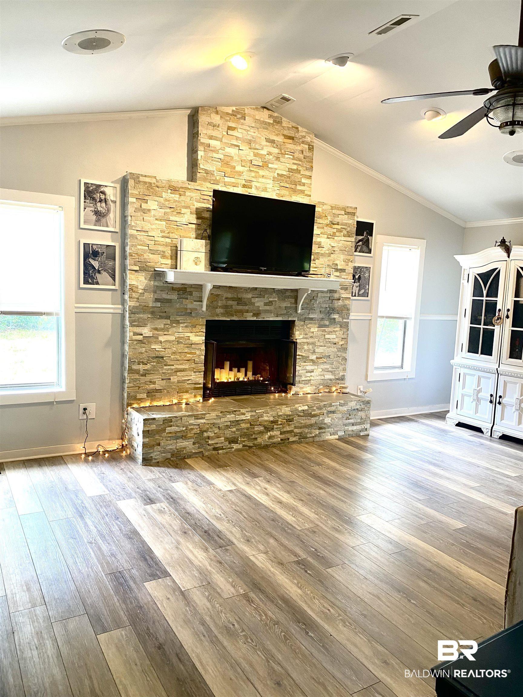 Image 2: Living space featuring a stacked stone fireplace with a white mantel, wood-finish flooring, vaulted ceilings, and recessed lighting